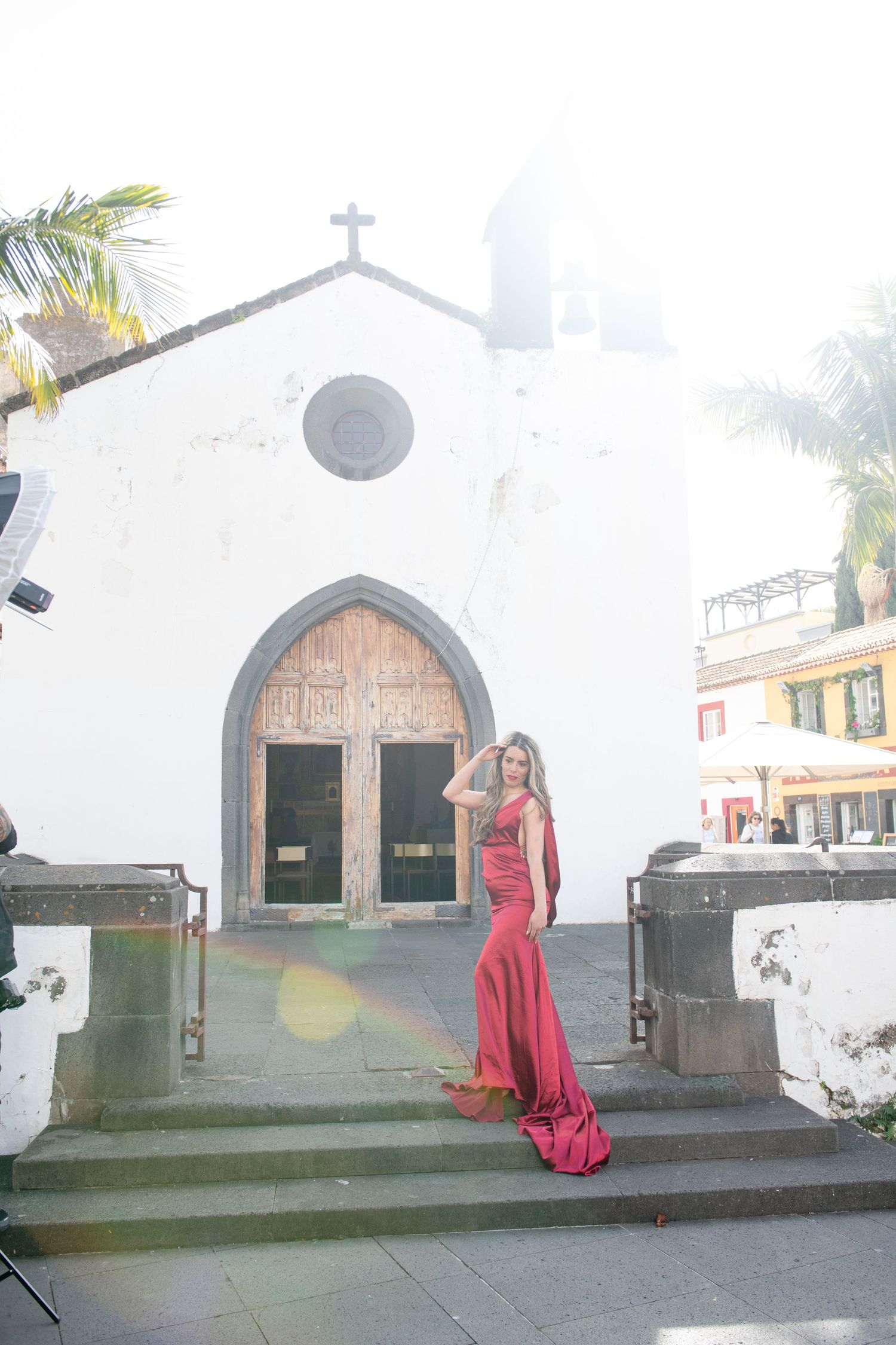 Small white church with arched doorway and cross on top surrounded by palm trees.