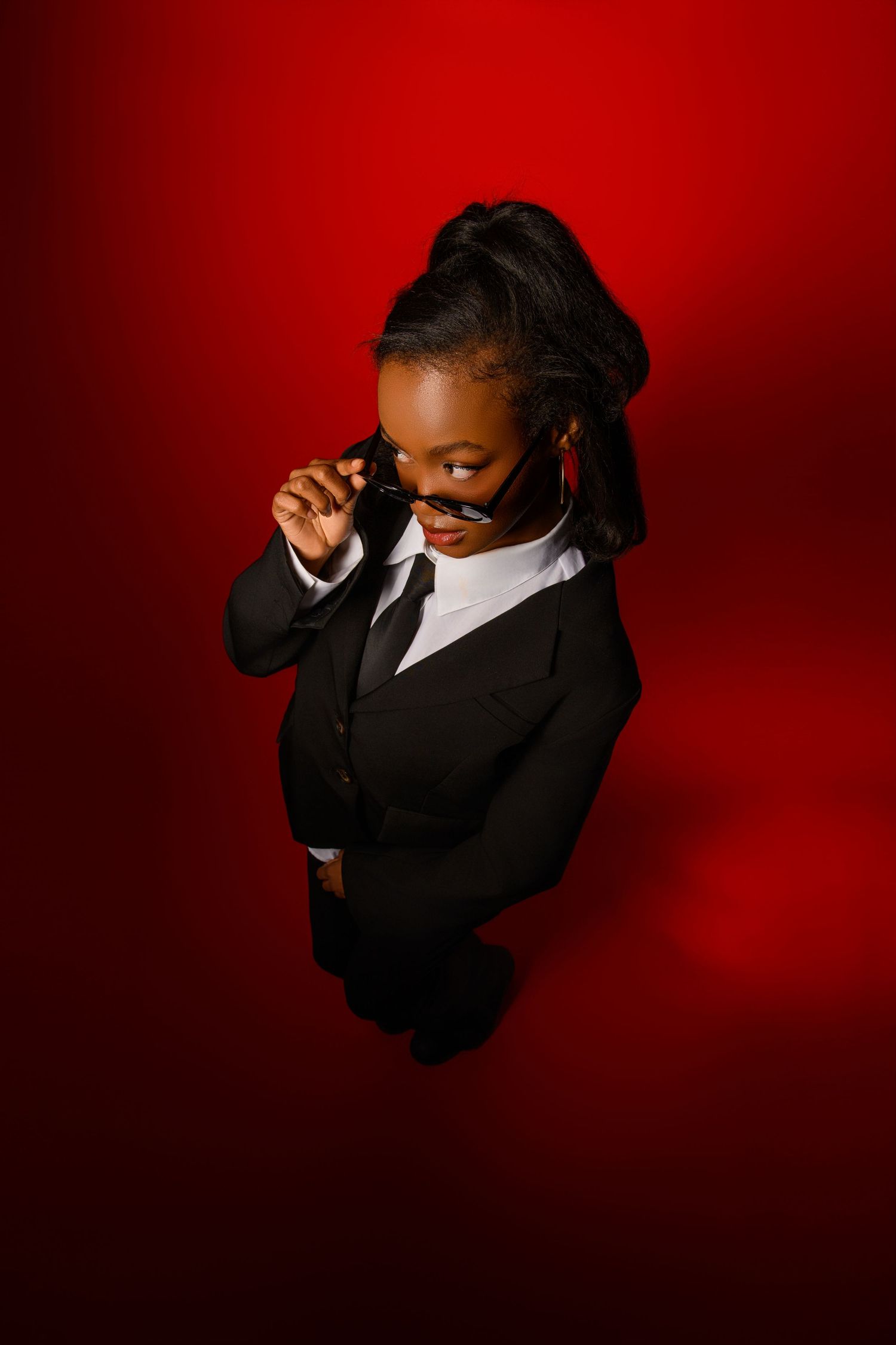 Professional wearing black suit and tie poses dramatically against red backdrop.
