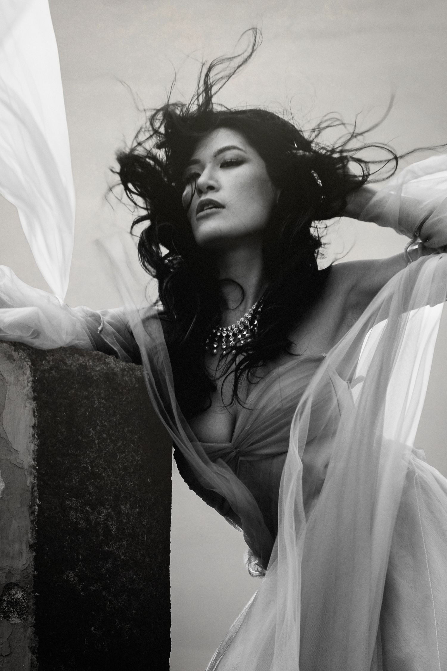 Dramatic black and white portrait with billowing sheer fabric and statement jewelry.