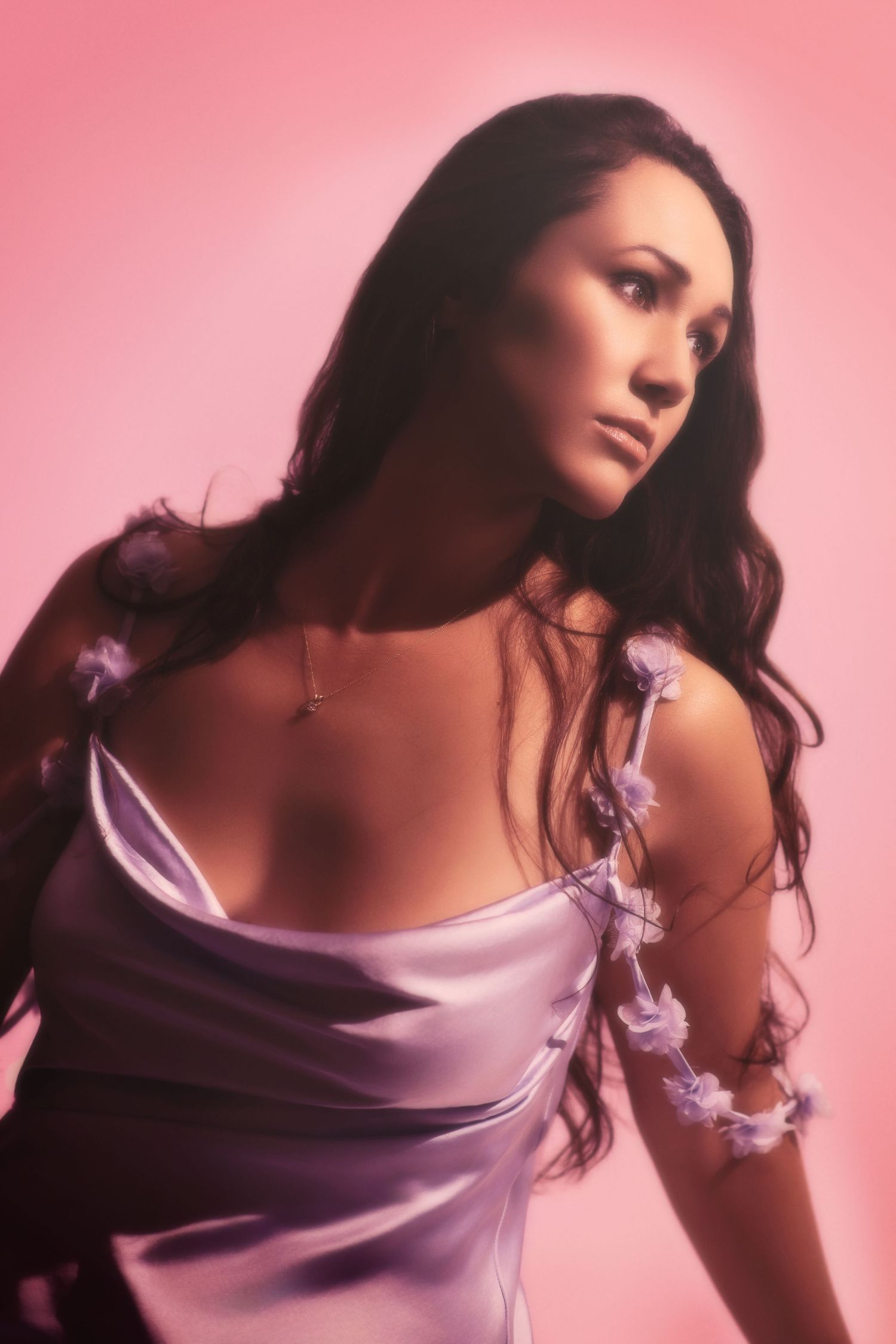 Fashion portrait of a woman in pink lighting wearing a romantic satin dress with floral details. Elegant boudior