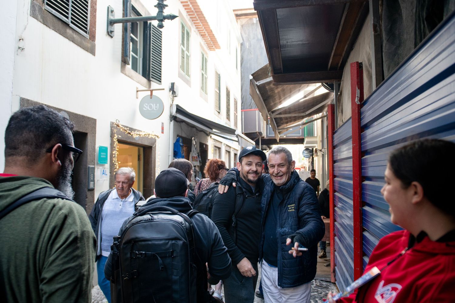 Crowd of tourists walking through narrow street lined with buildings and shops.