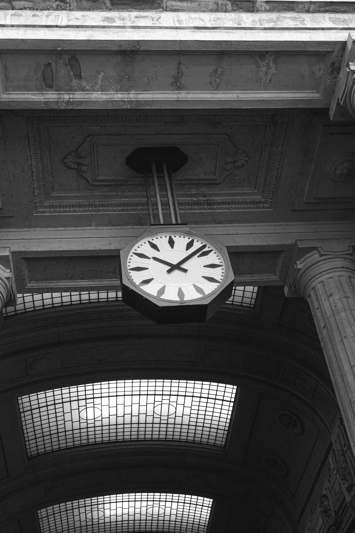 Low angle view of a vintage clock mounted on an ornate ceiling with skylights.