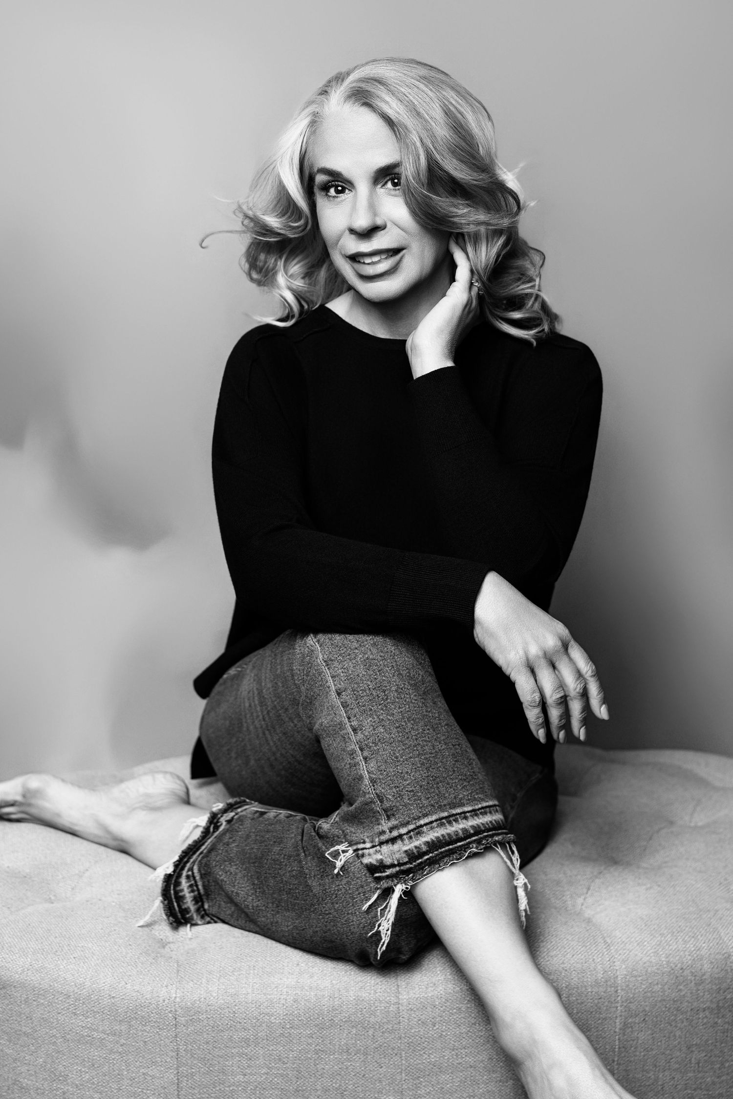 Black and white portrait of someone in casual attire seated on furniture.