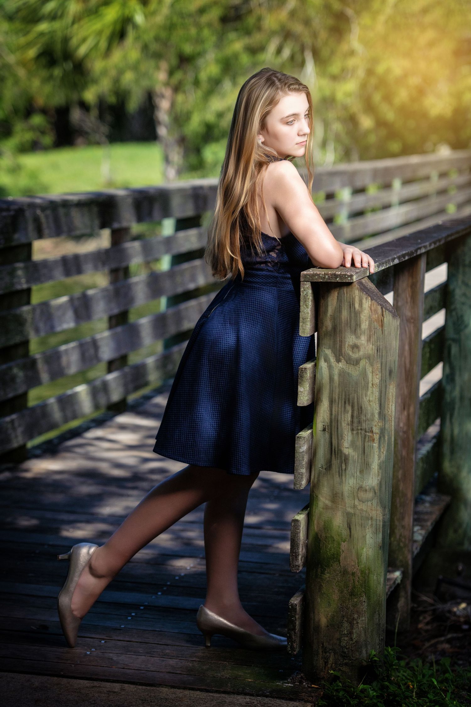 Multiple poses of someone in a navy dress leaning on a rustic wooden fence.