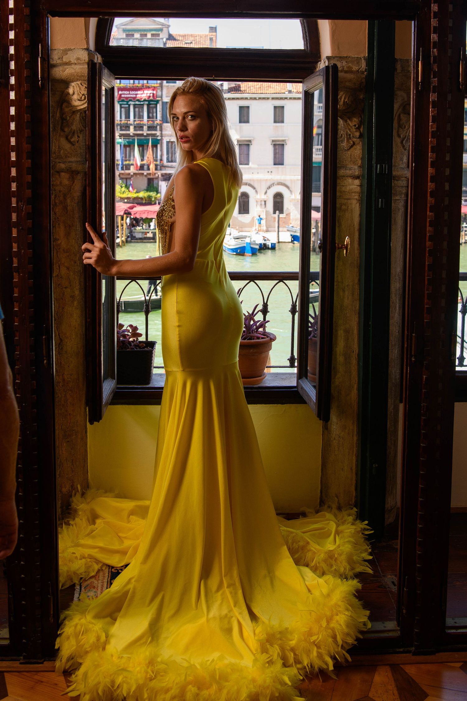 Yellow mermaid gown with feather trim photographed in Venetian window frame.
