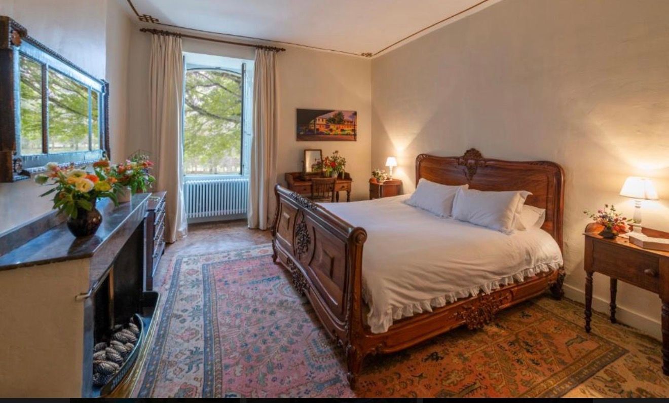 Elegant bedroom with ornate wooden sleigh bed, Persian rug, warm lighting, and large window with garden views.