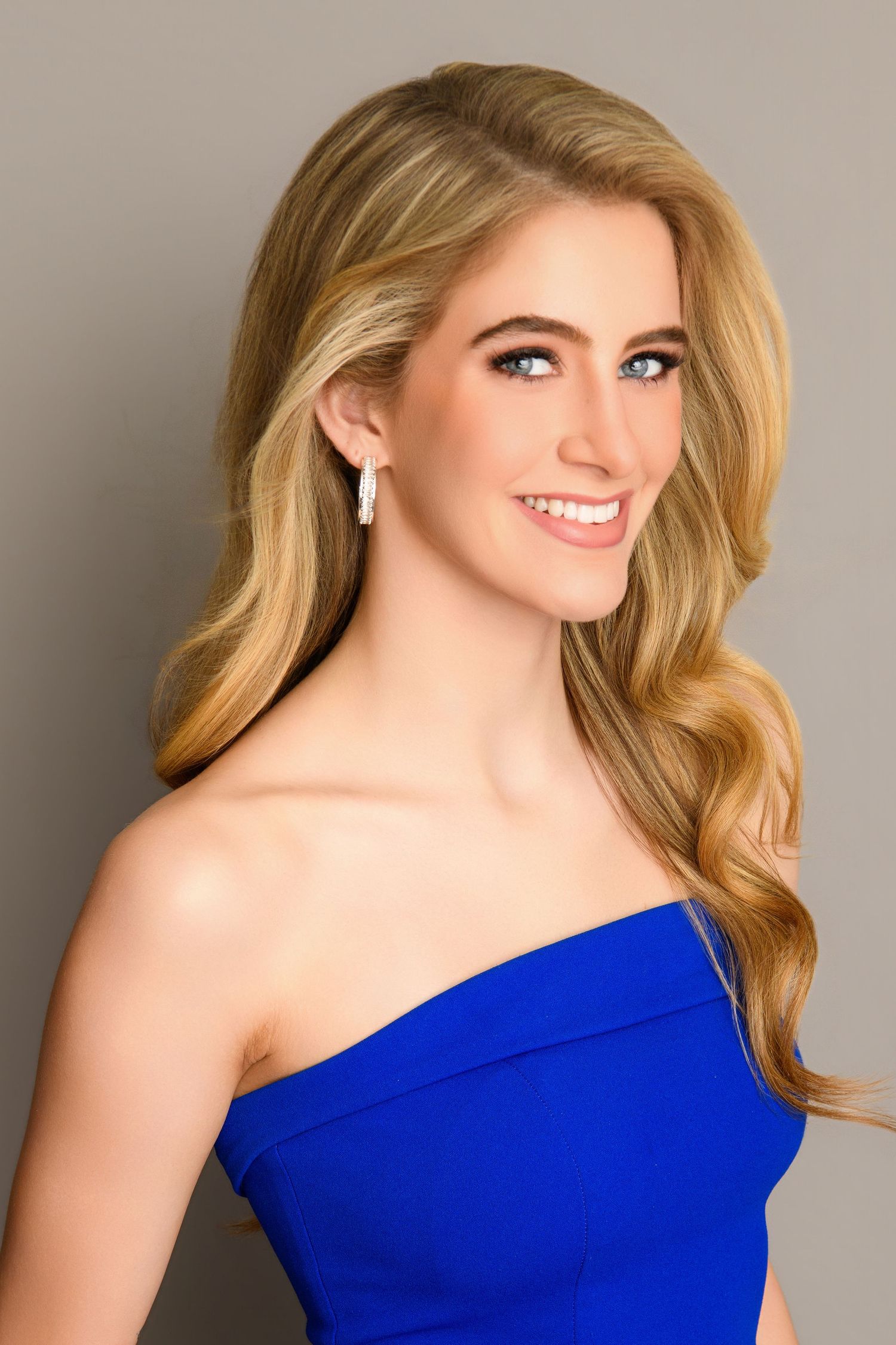 A one-shoulder royal blue evening dress is showcased in a glamorous portrait series against a gray backdrop.