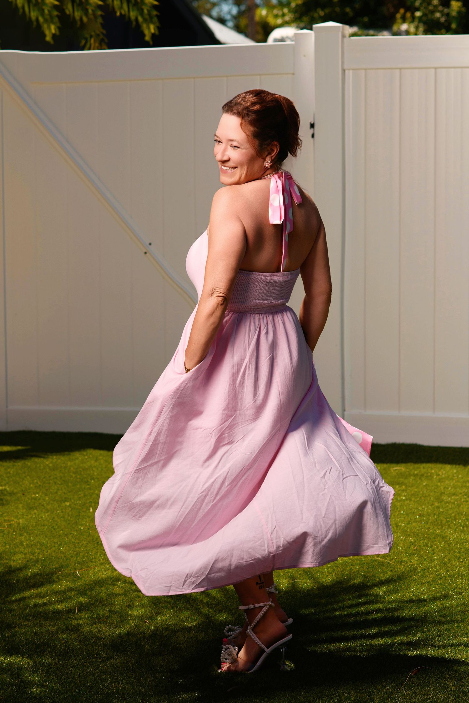 Playful outdoor photoshoot featuring flowing pink dress movements against a white fence.