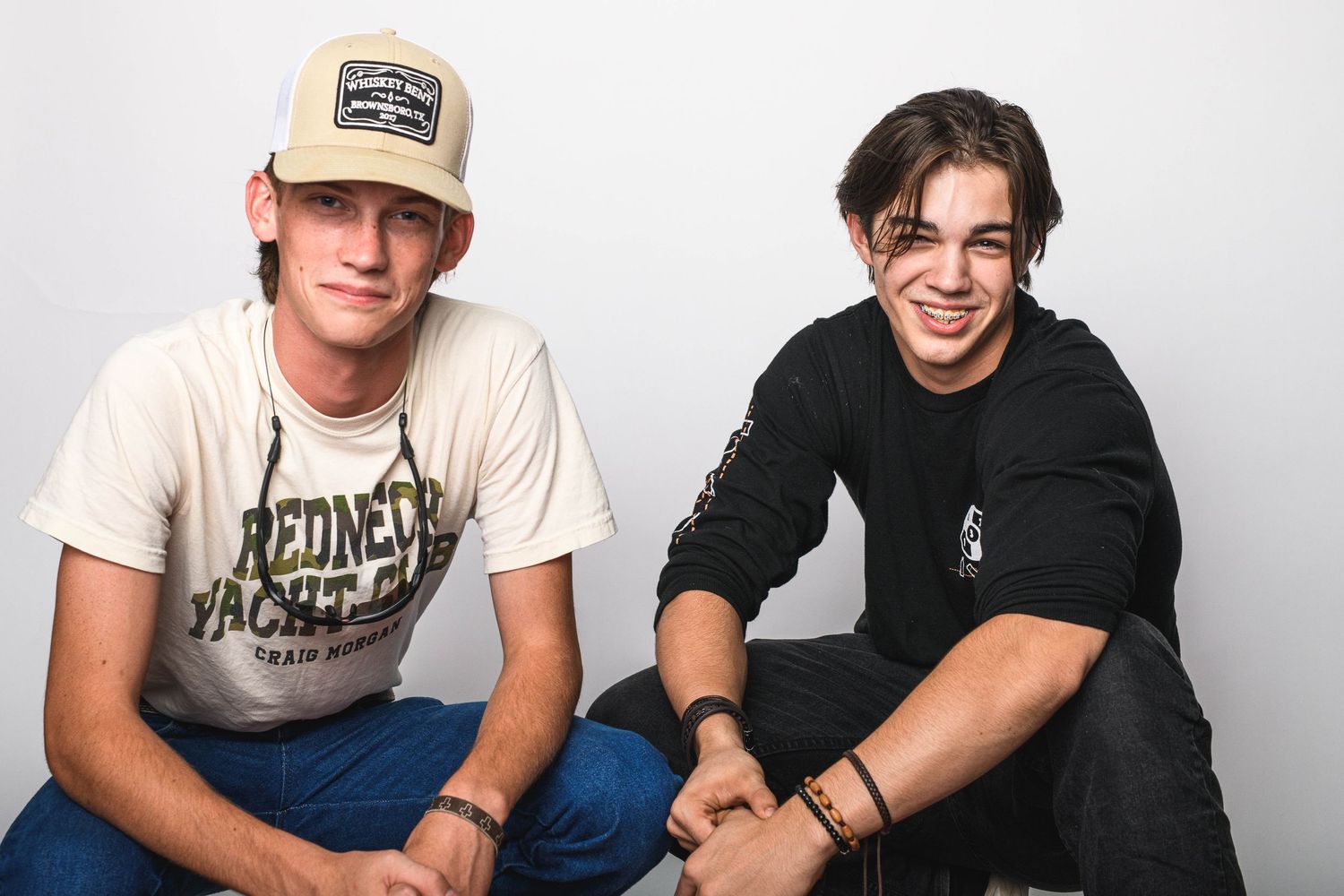 Two people sitting casually together, one in baseball cap and vintage tee, other in black sweater.