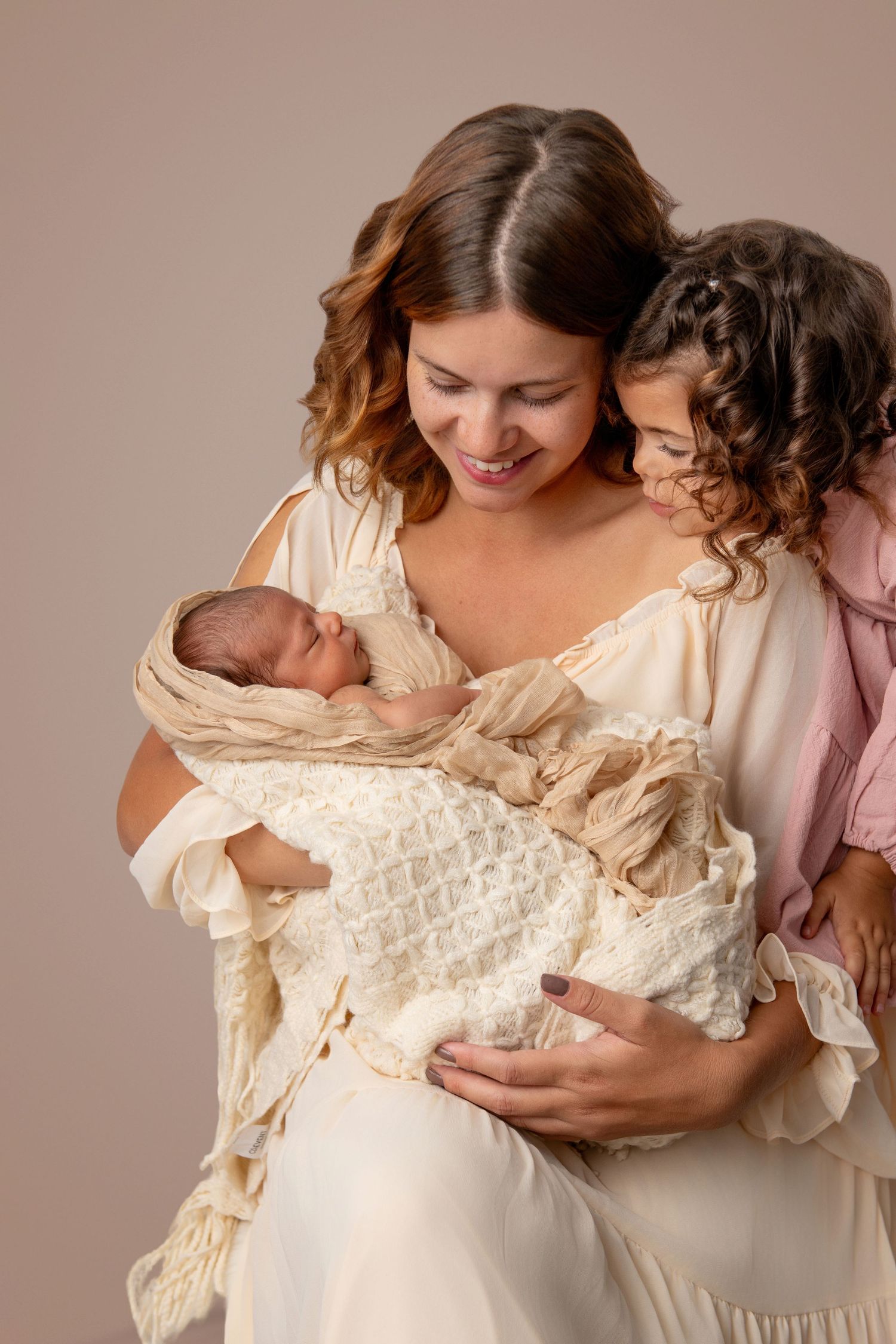 Tender moments between mother and children in cream-colored clothing against neutral backdrop.