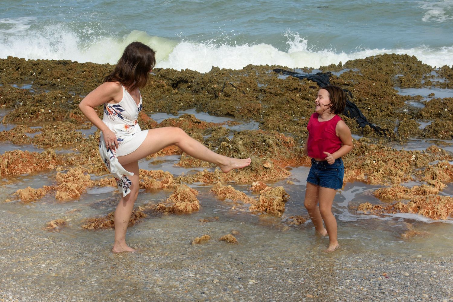 Two people playing and running along a rocky beach shoreline.
