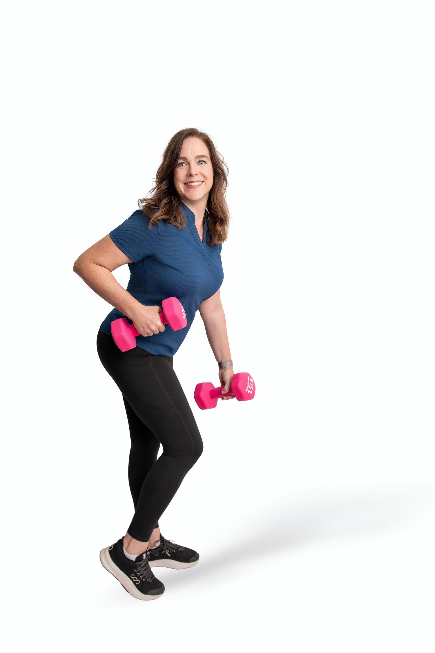 Person exercising with pink dumbbells while wearing navy top and black pants against white backdrop.