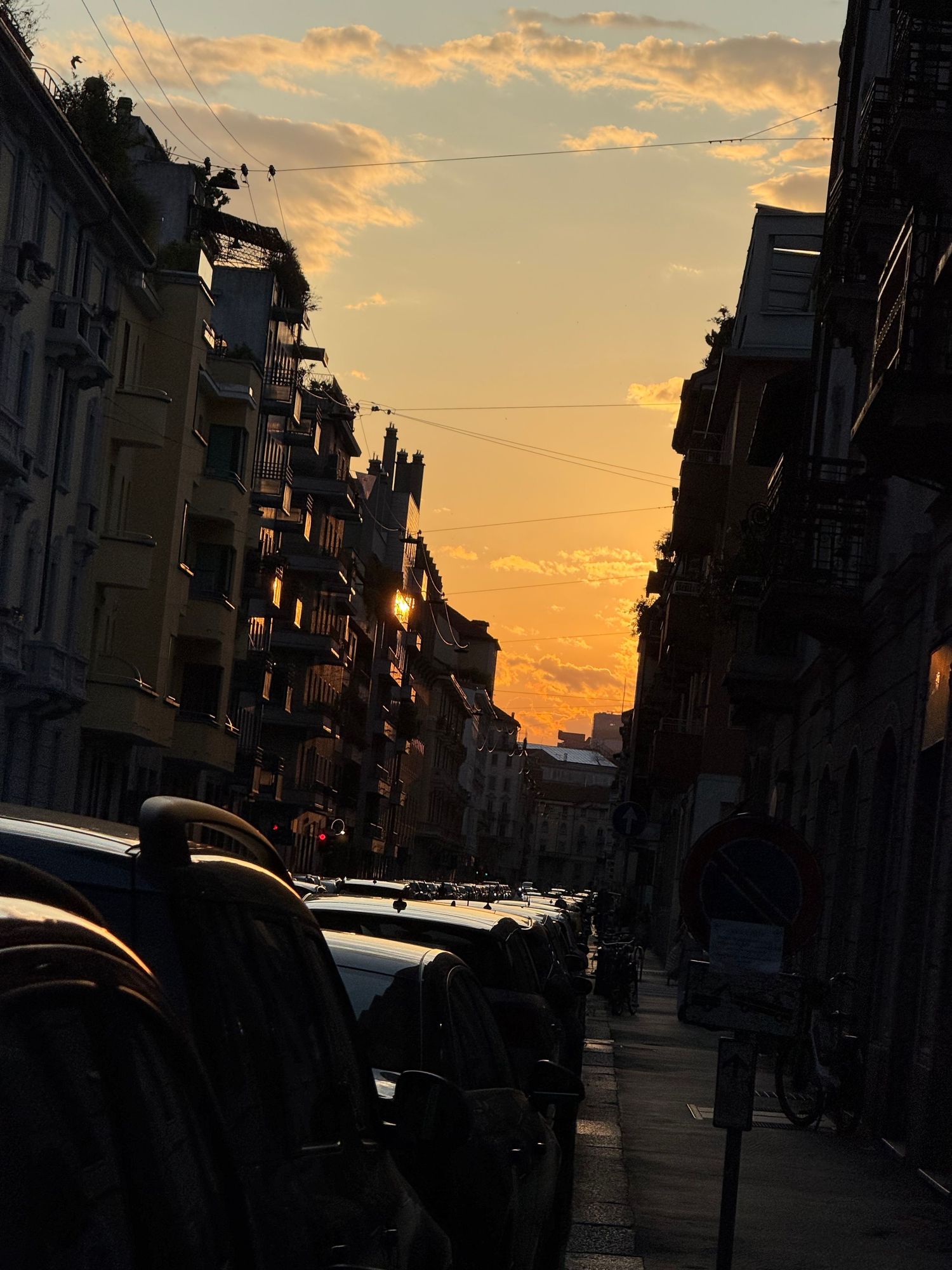 Urban street scene at sunset with silhouetted buildings and warm sky.