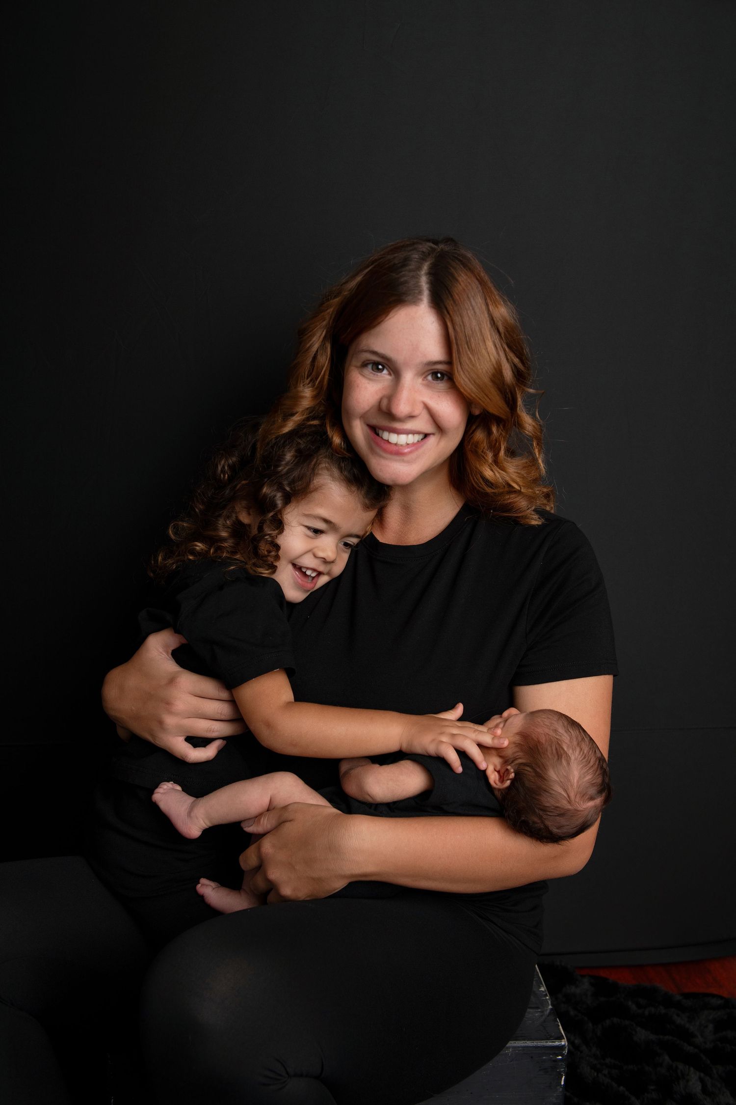 Family portrait series in black and white showing joyful embraces and laughter against dark background.