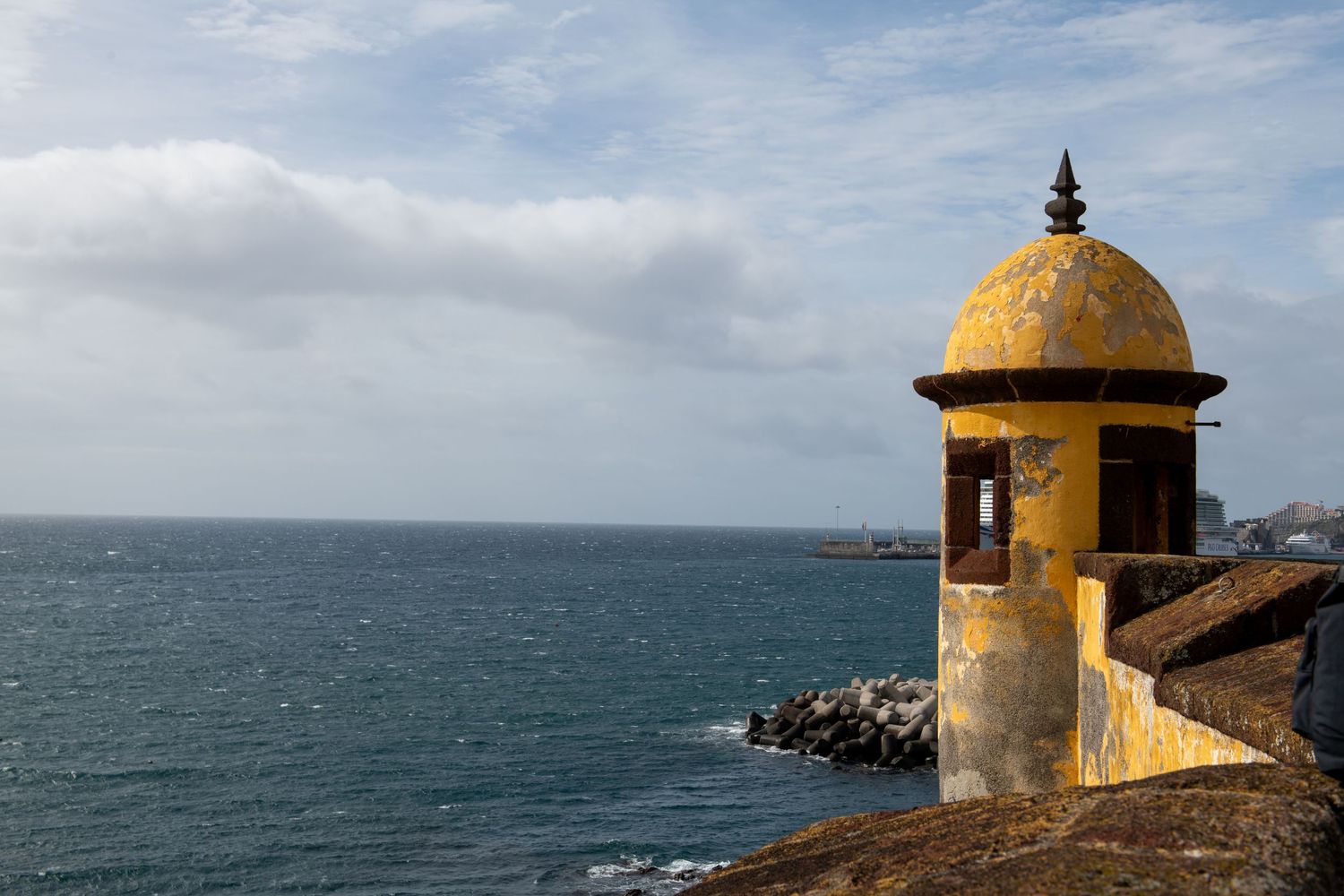 Historic yellow watchtower overlooking ocean with cloudy sky in background.