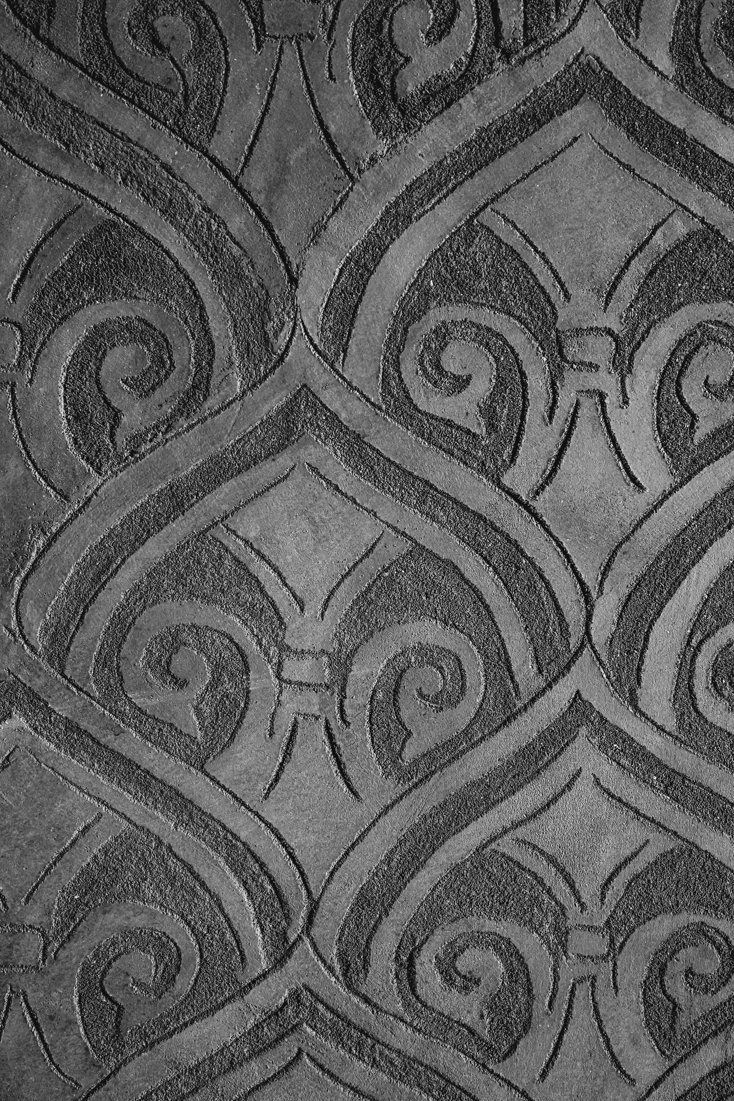 Grayscale close-up of ornate architectural pattern showing repeating swirls and geometric designs.
