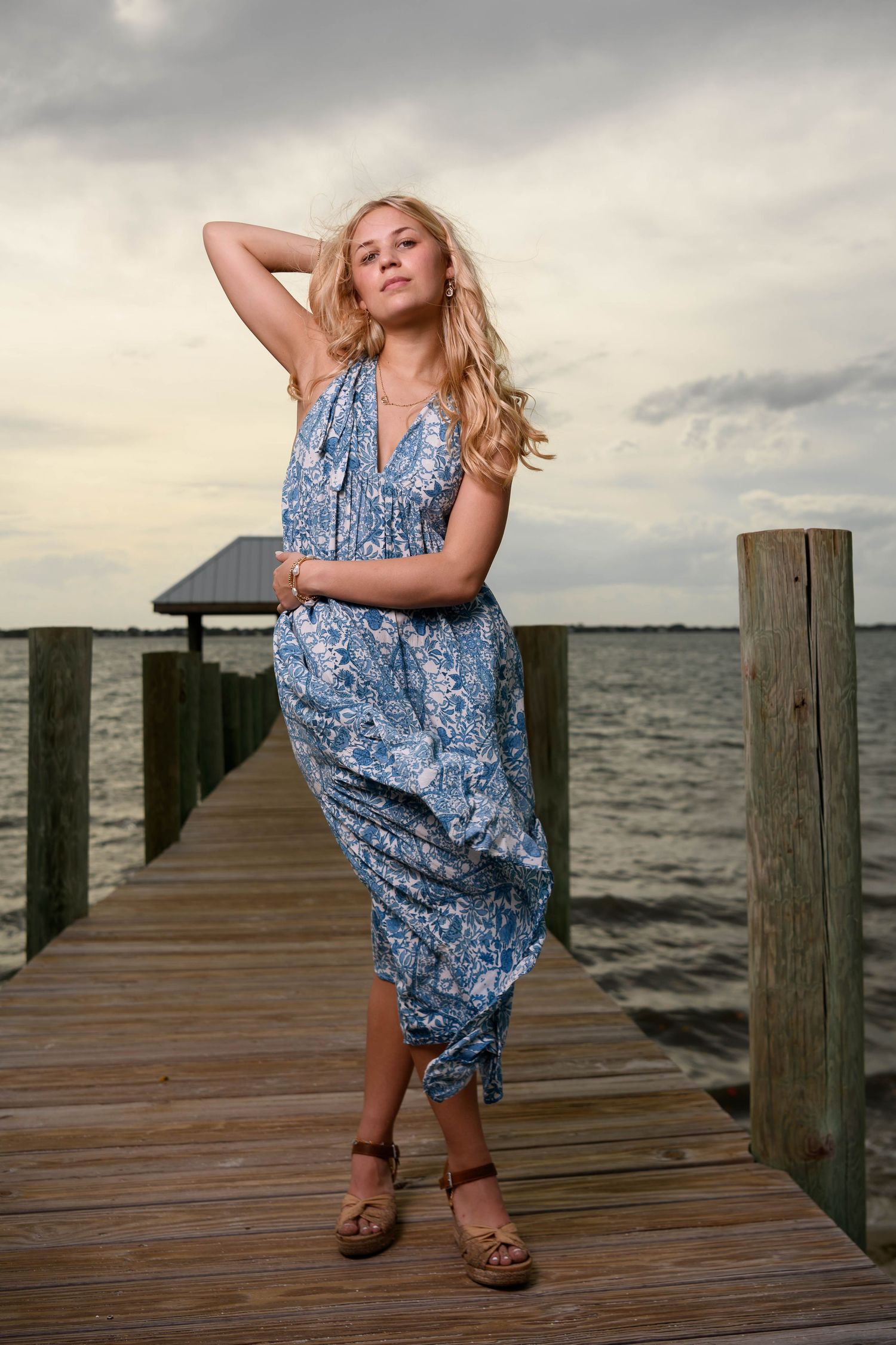 Casual pose in blue maxi dress on waterfront pier during golden hour.