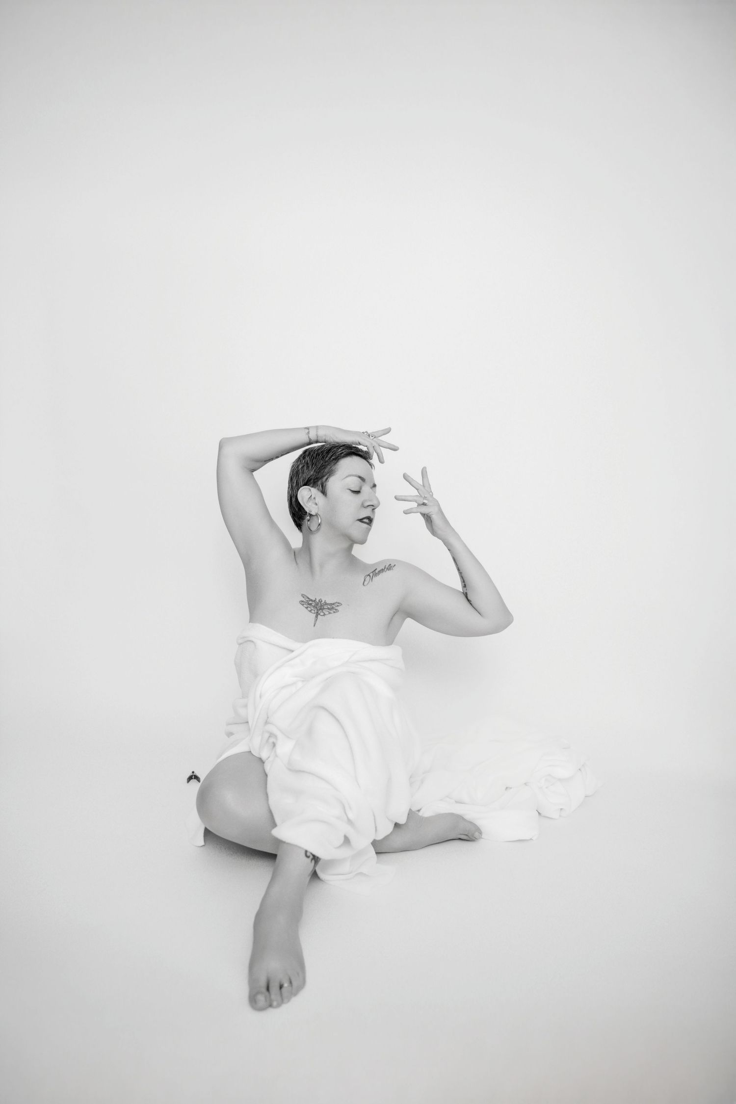 Artistic black and white photo of a figure reclining in white fabric with dramatic lighting.