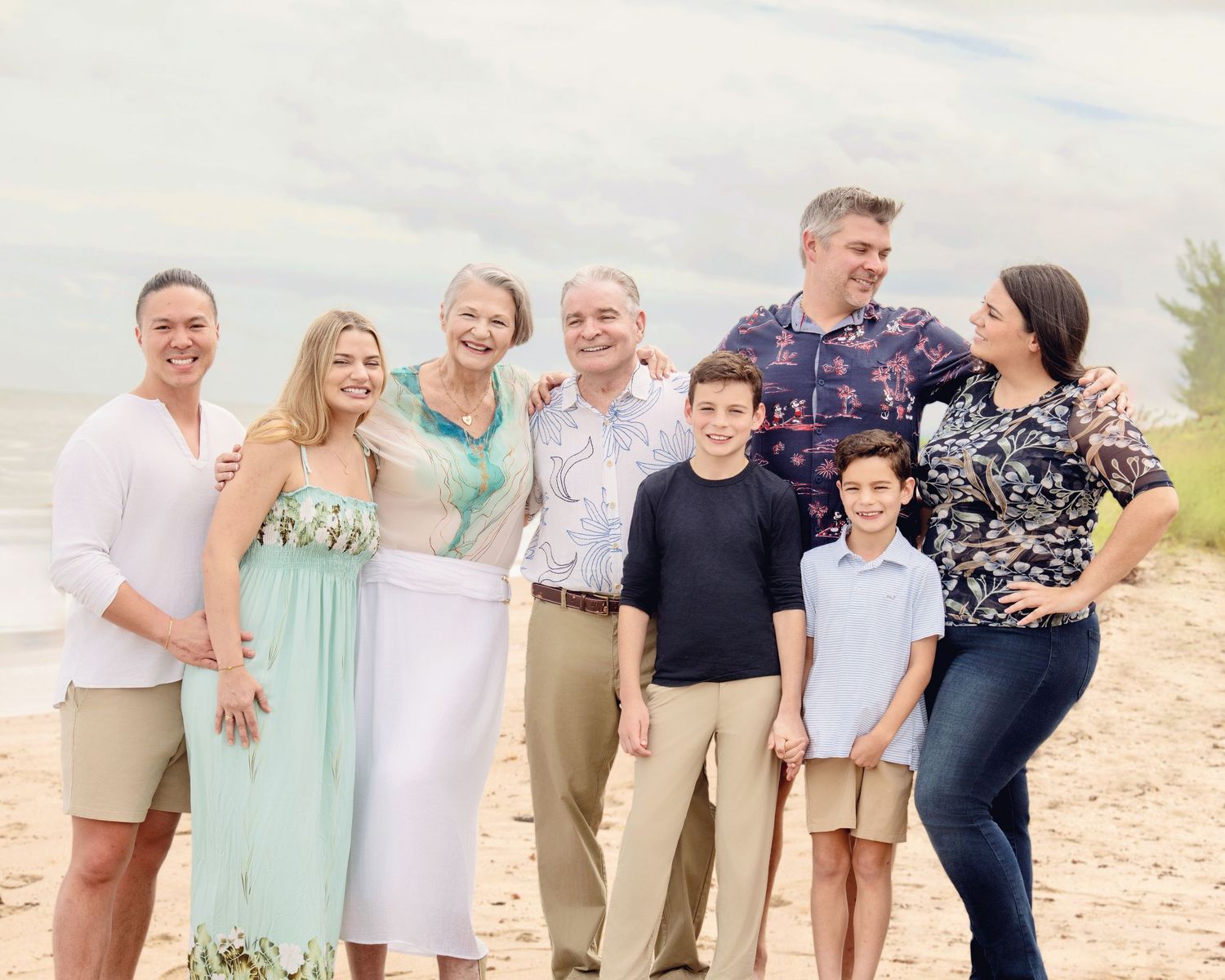 Multi-generational family photo session on sandy beach with ocean backdrop.