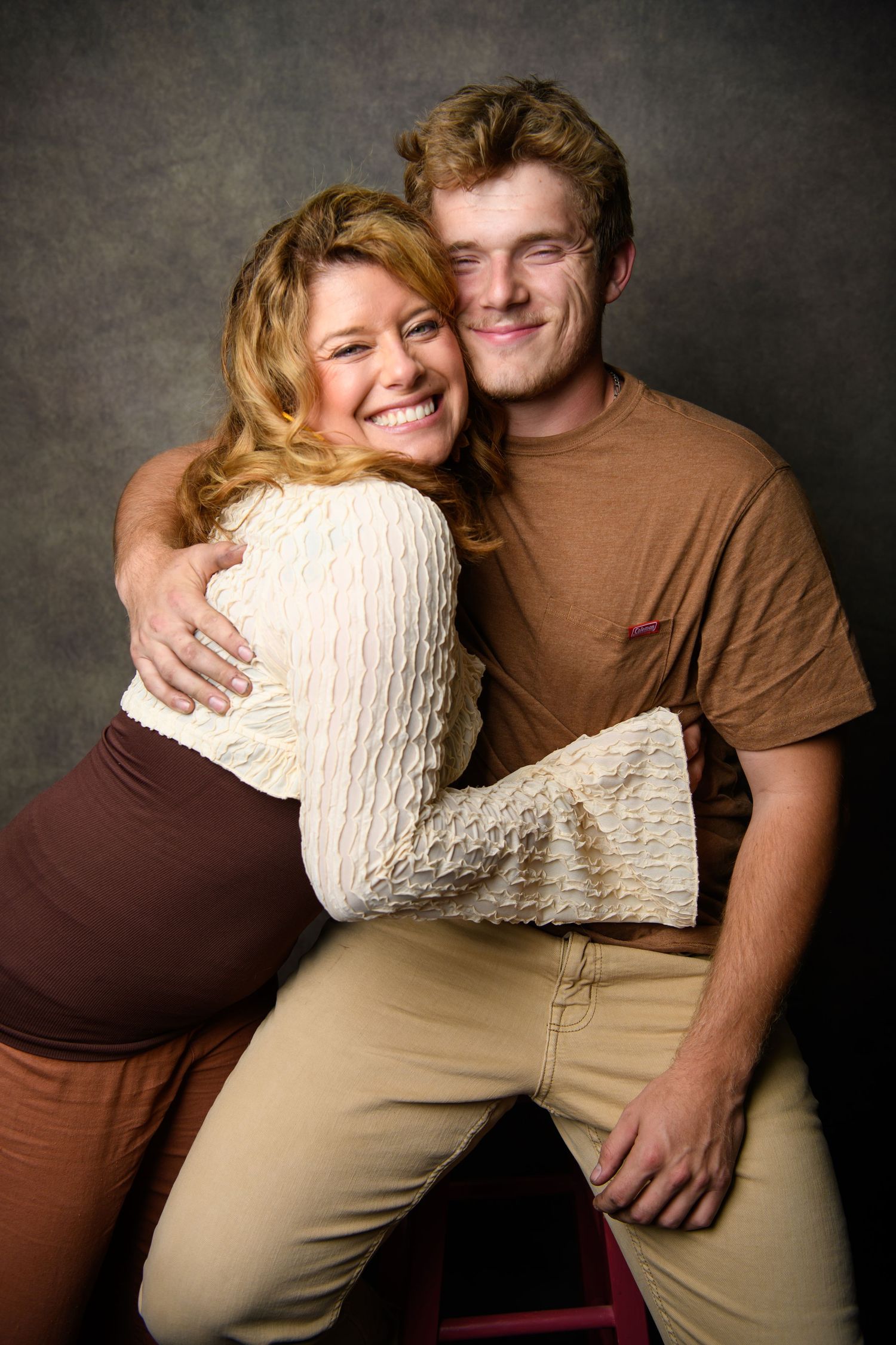 Couple in casual attire embracing and smiling against dark backdrop in romantic portrait series.