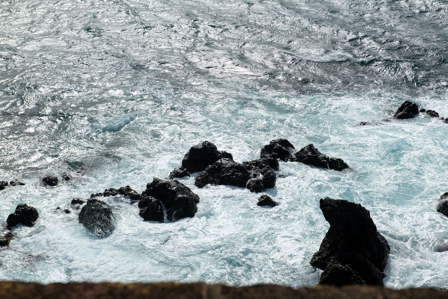 Dramatic rocky coastline with crashing waves against black volcanic rocks and white sea foam.