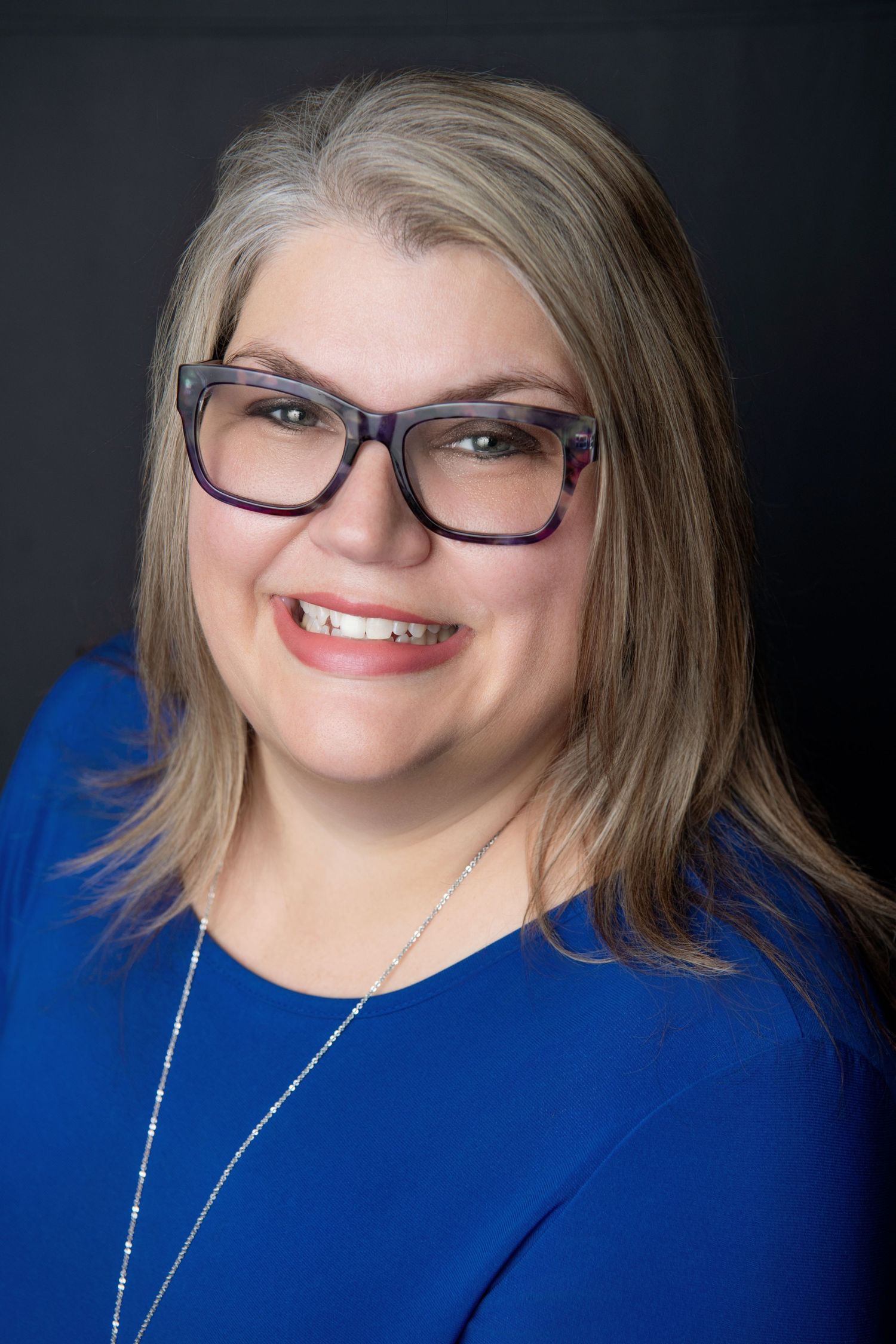 Professional portrait of a woman in blue top wearing stylish glasses.
