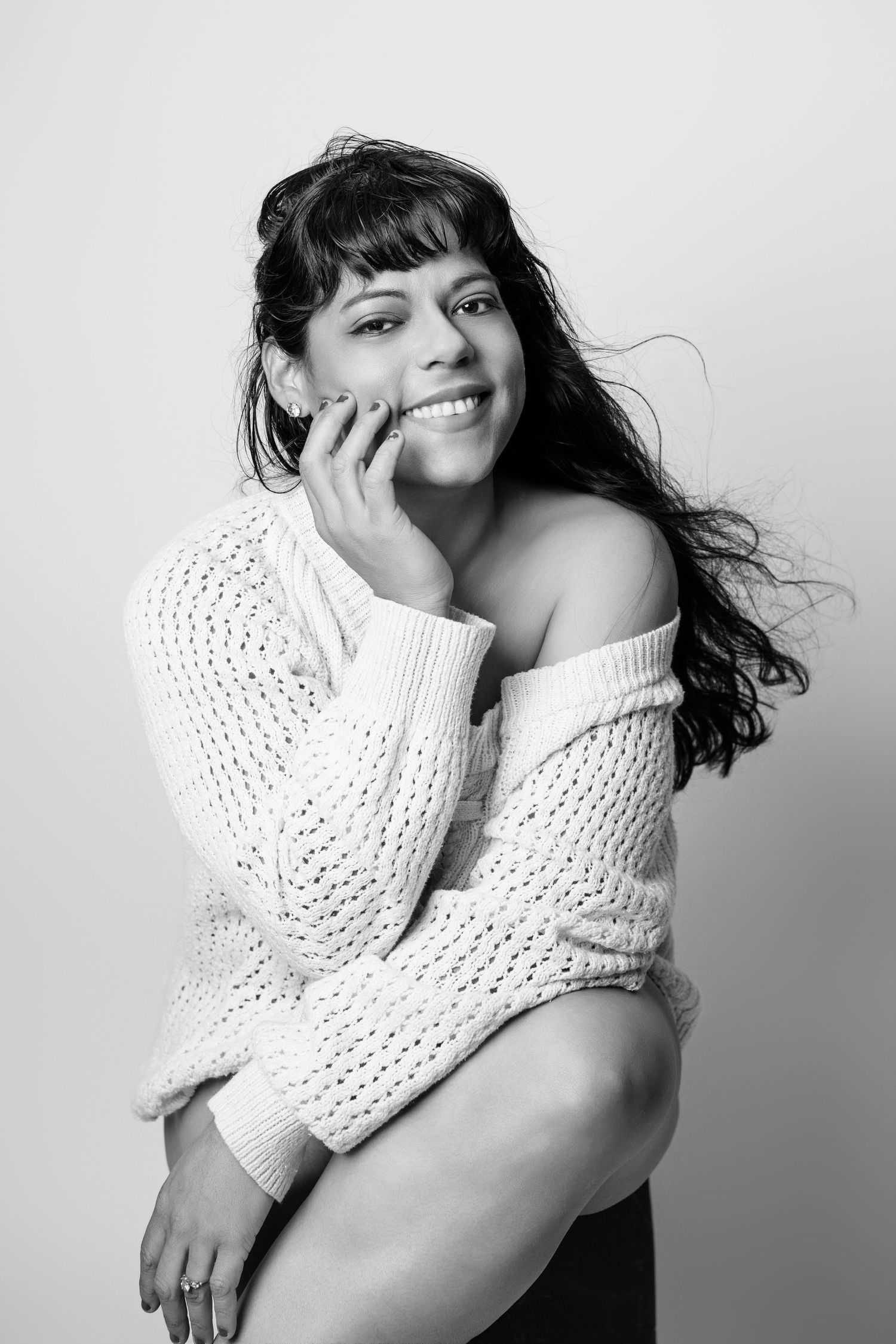 Woman in white knit sweater poses playfully in black and white studio portraits.