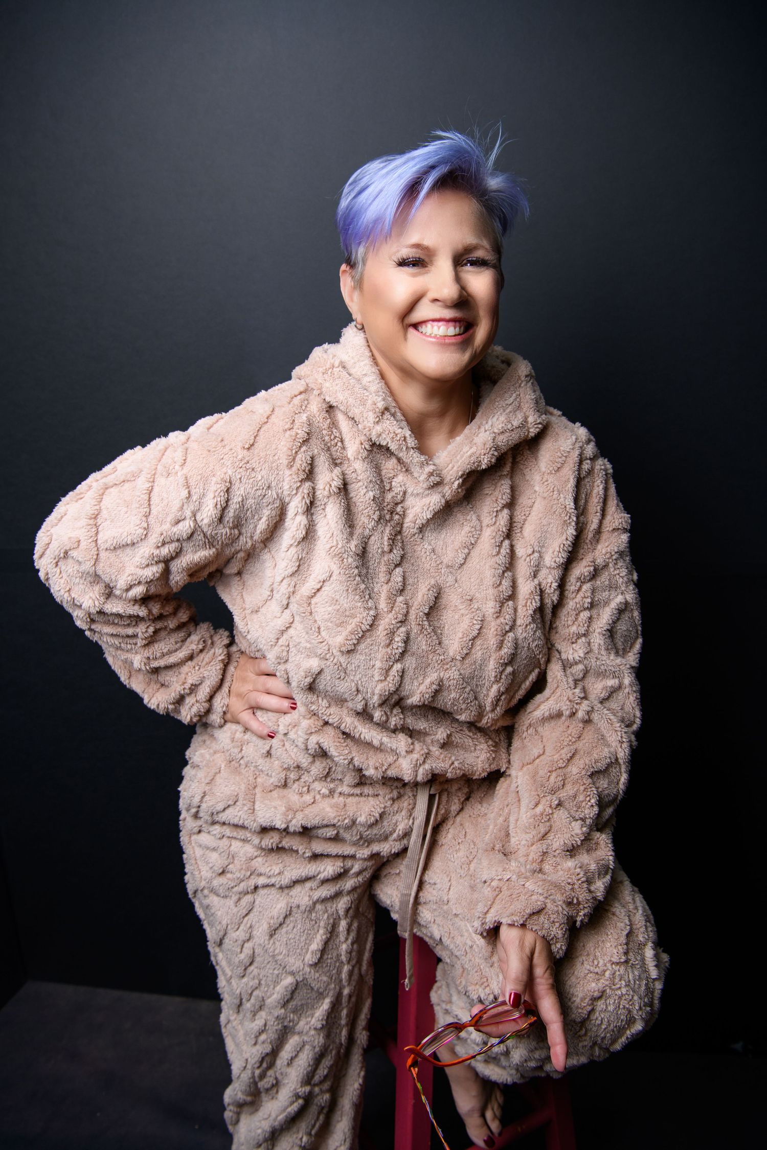 Playful studio shots wearing plush beige coat against dark background.