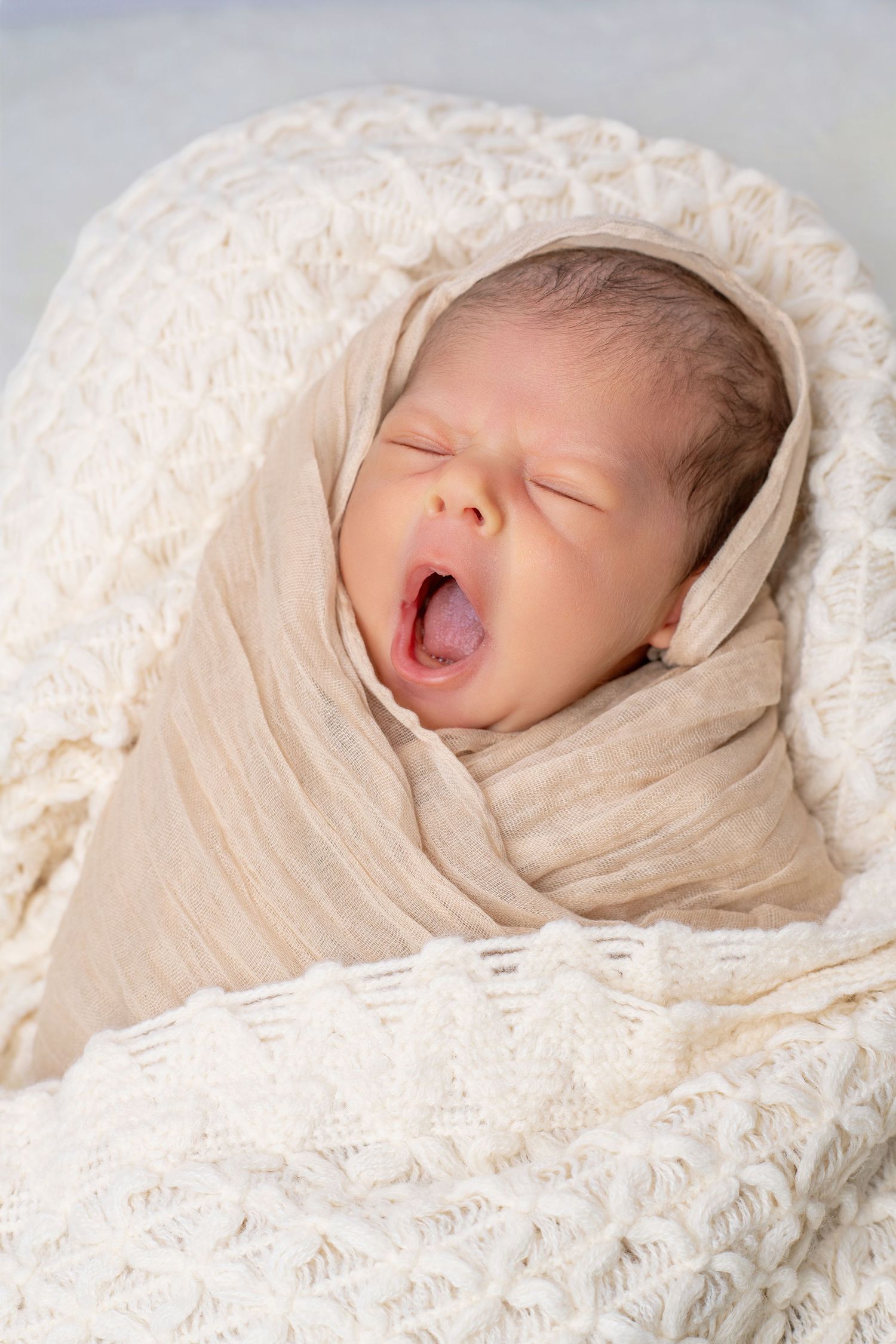 Series of peaceful sleeping newborn wrapped in cream blanket showing different expressions.