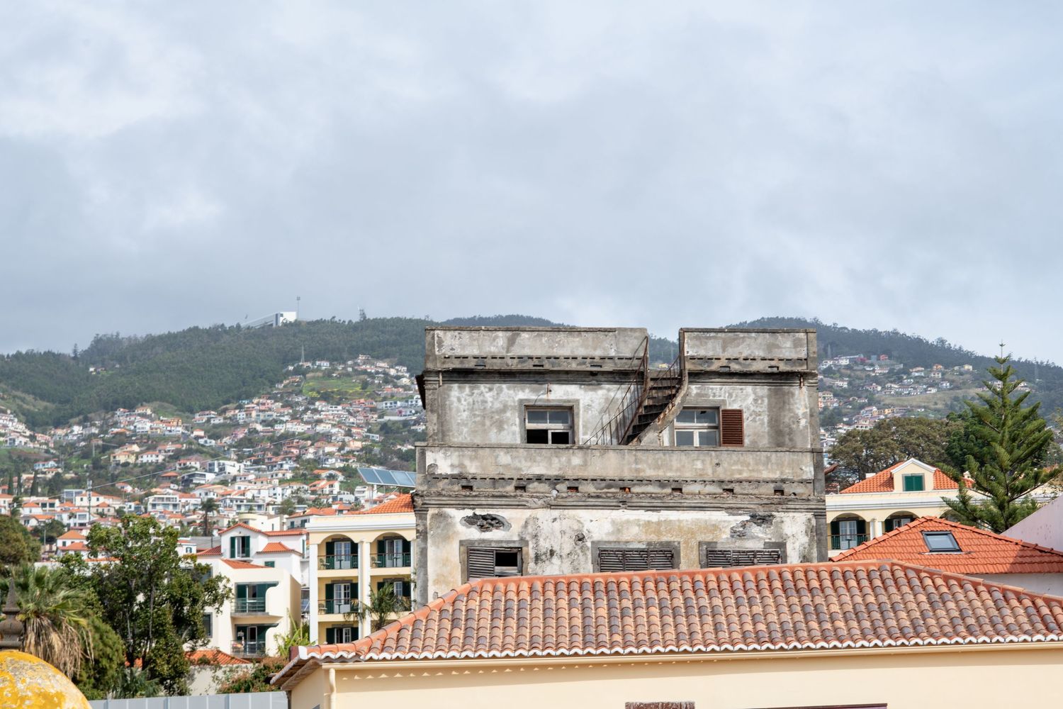 Panoramic cityscape view of coastal town with terracotta roofs and mountains in background.