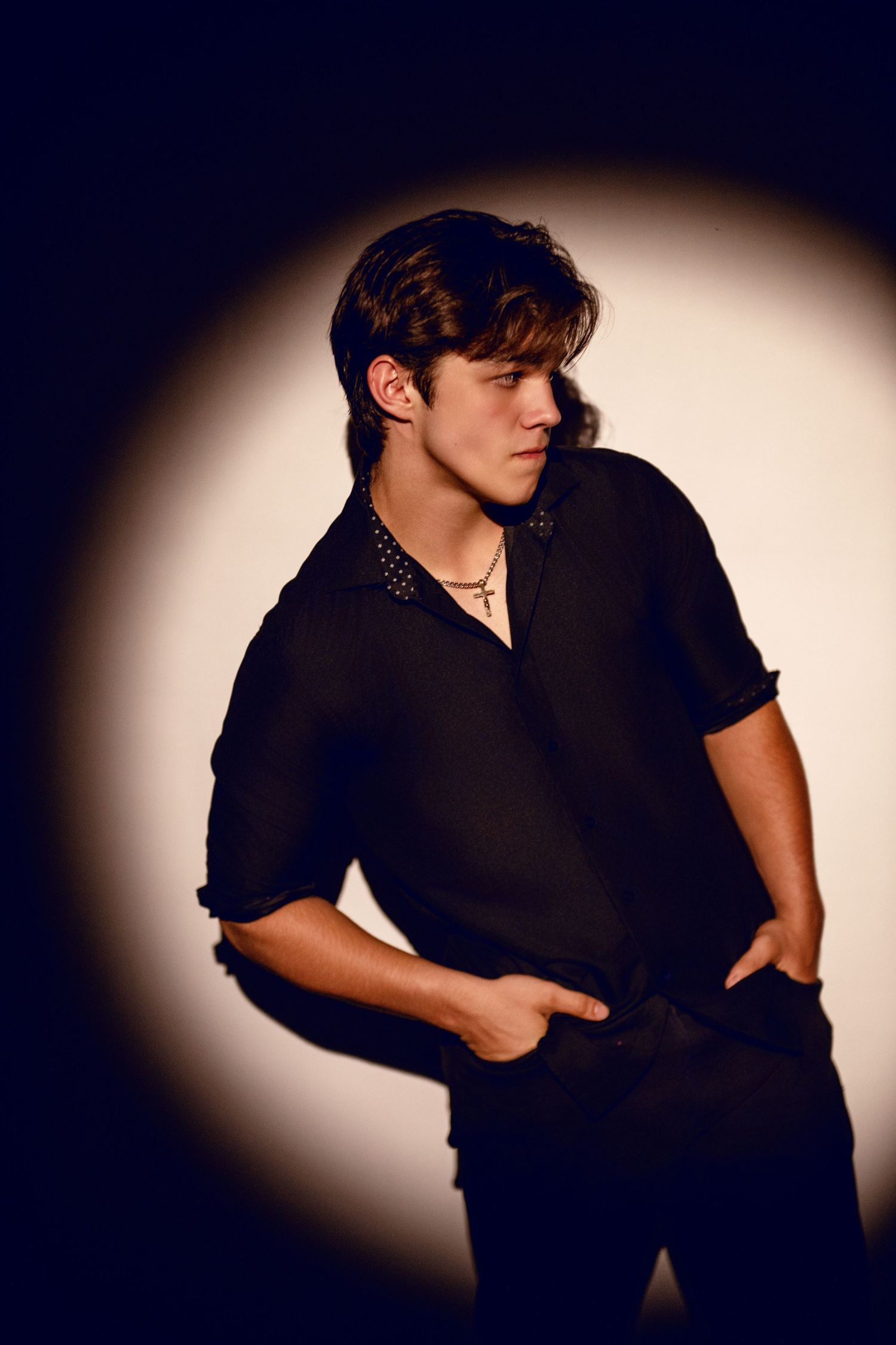 Dramatic studio portrait with person in black shirt against circular spotlight background.