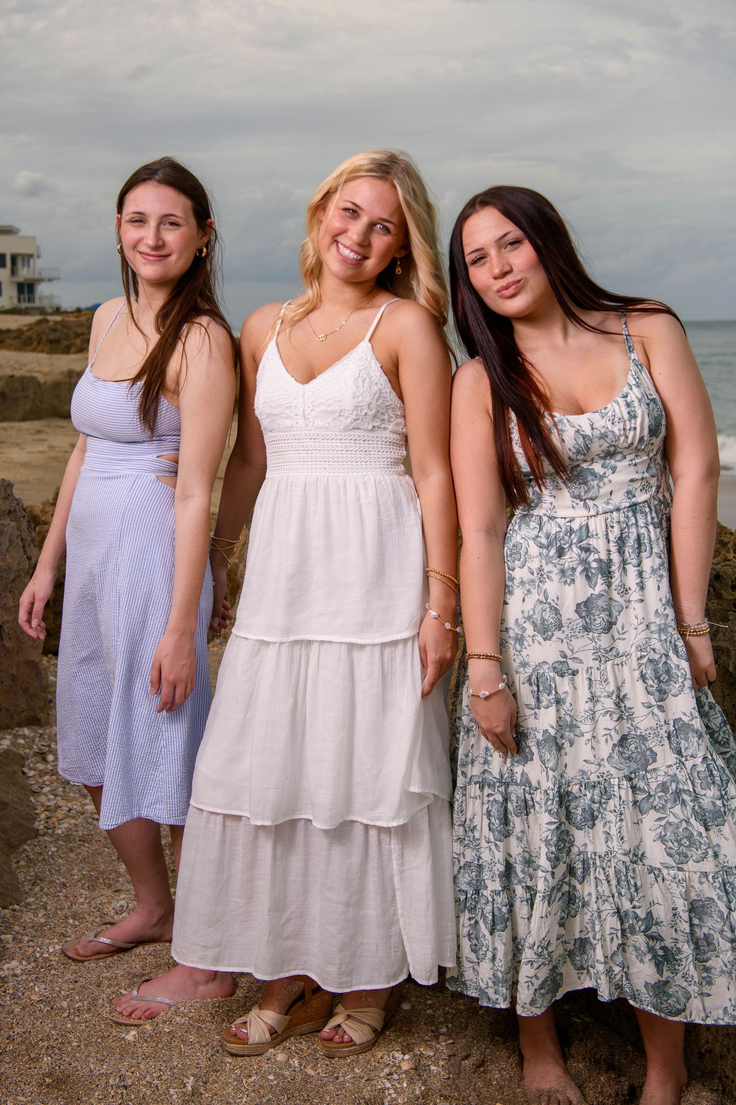 Three friends in summer dresses pose together on a beach at sunset, wearing casual maxi and midi length styles.