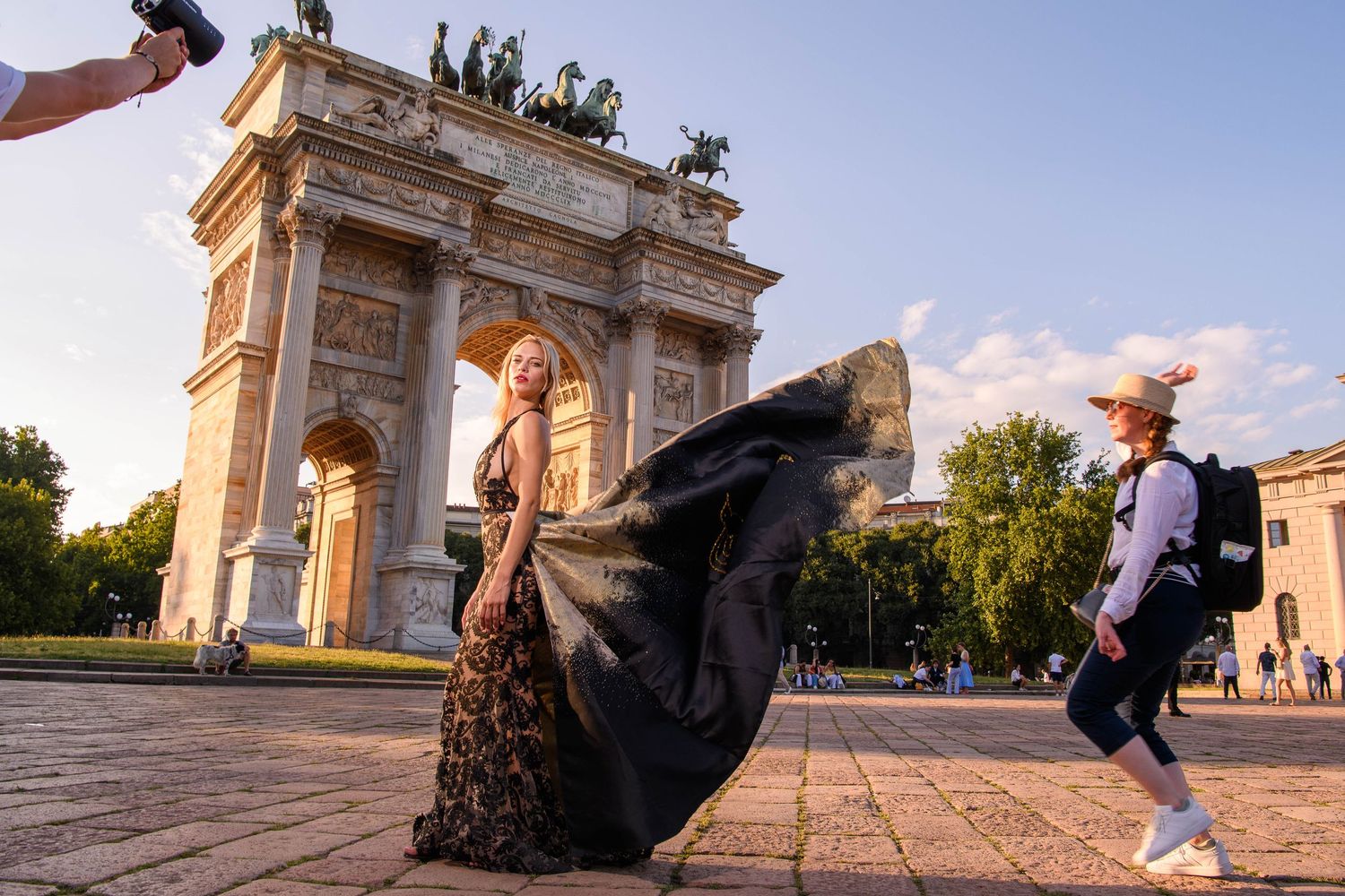 Wide angle view of people posing near grand architectural arch during golden hour.