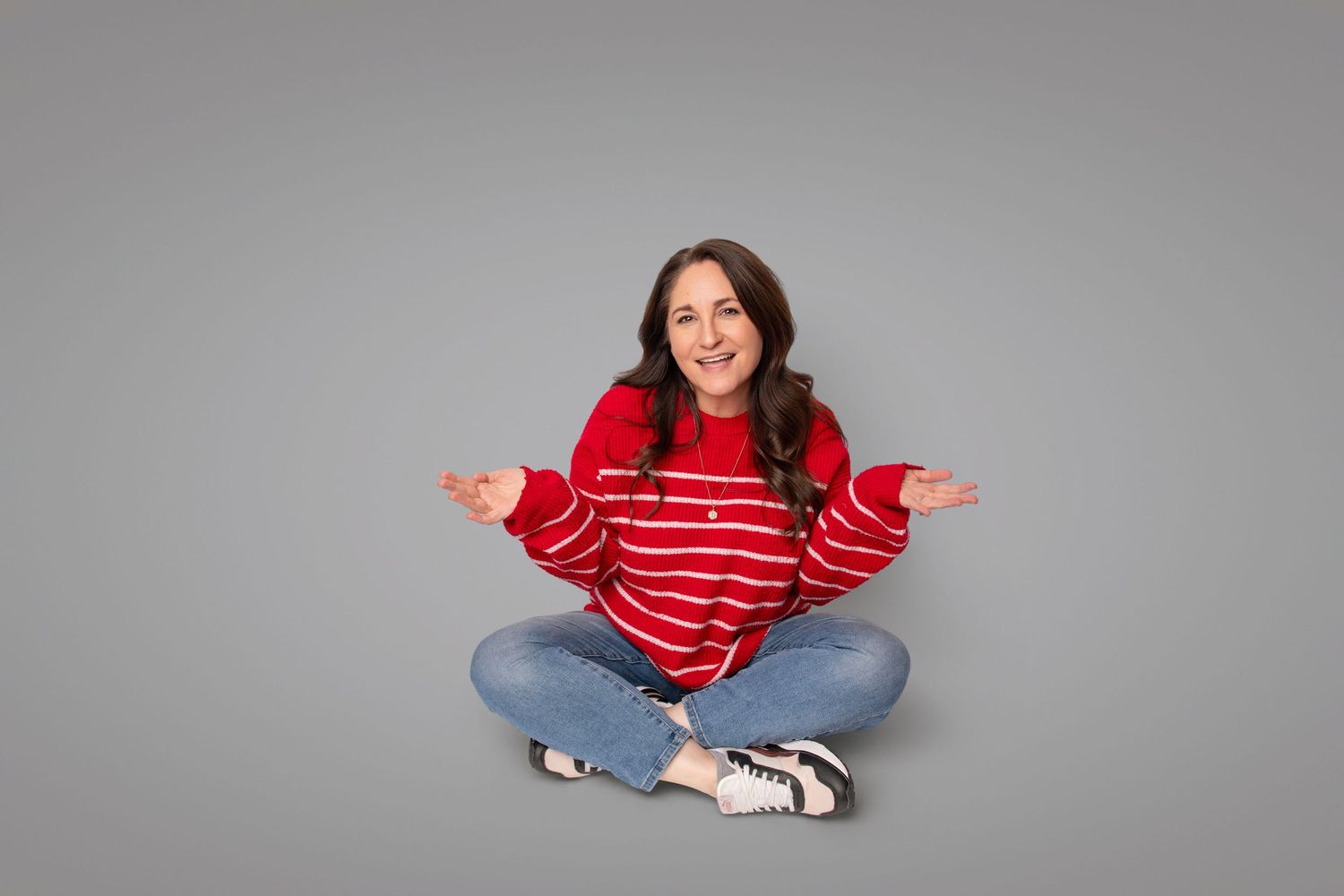 Casual poses in red striped sweater and jeans against neutral studio backdrop.