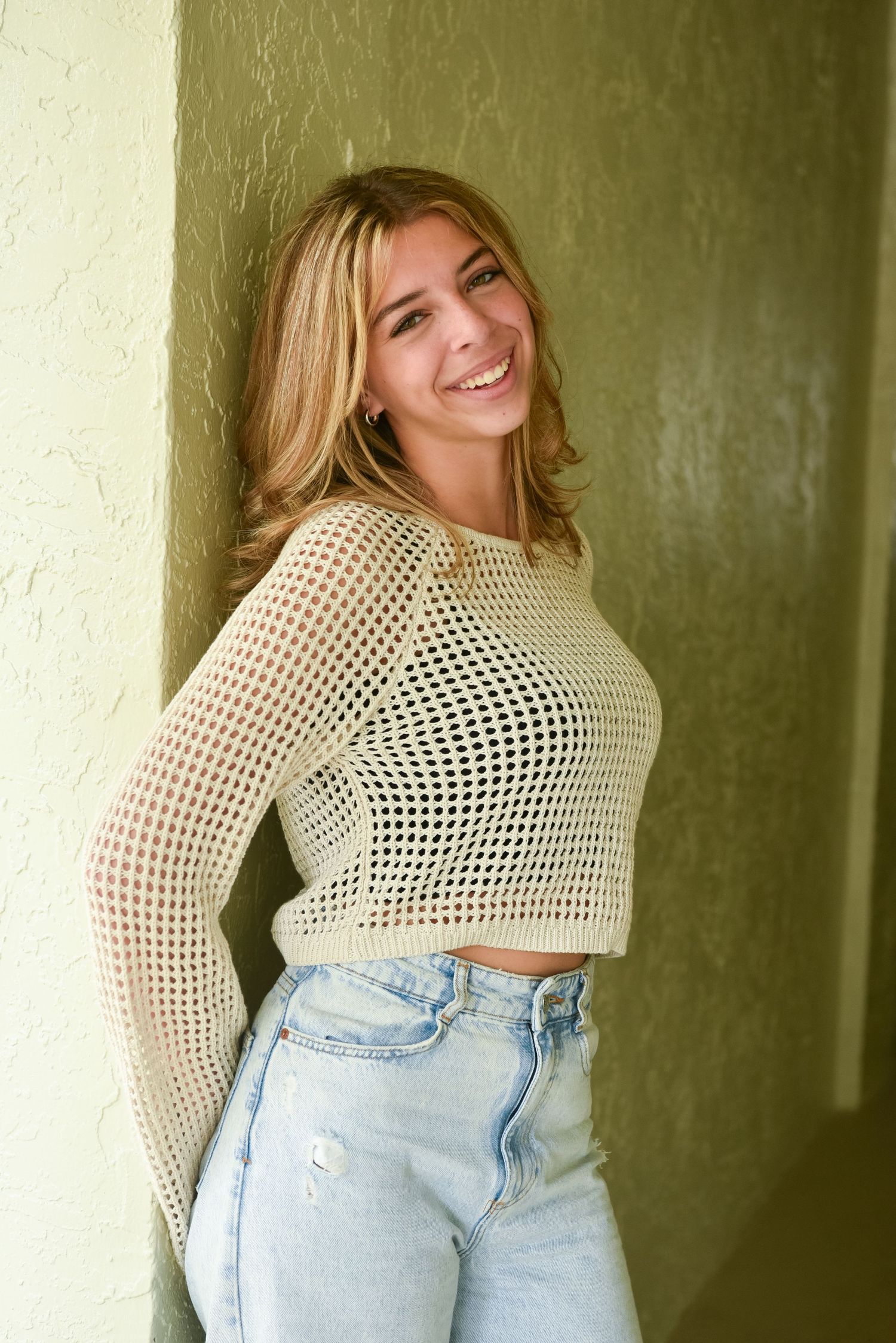 Series of poses in a white crochet top and light denim jeans against a green wall.