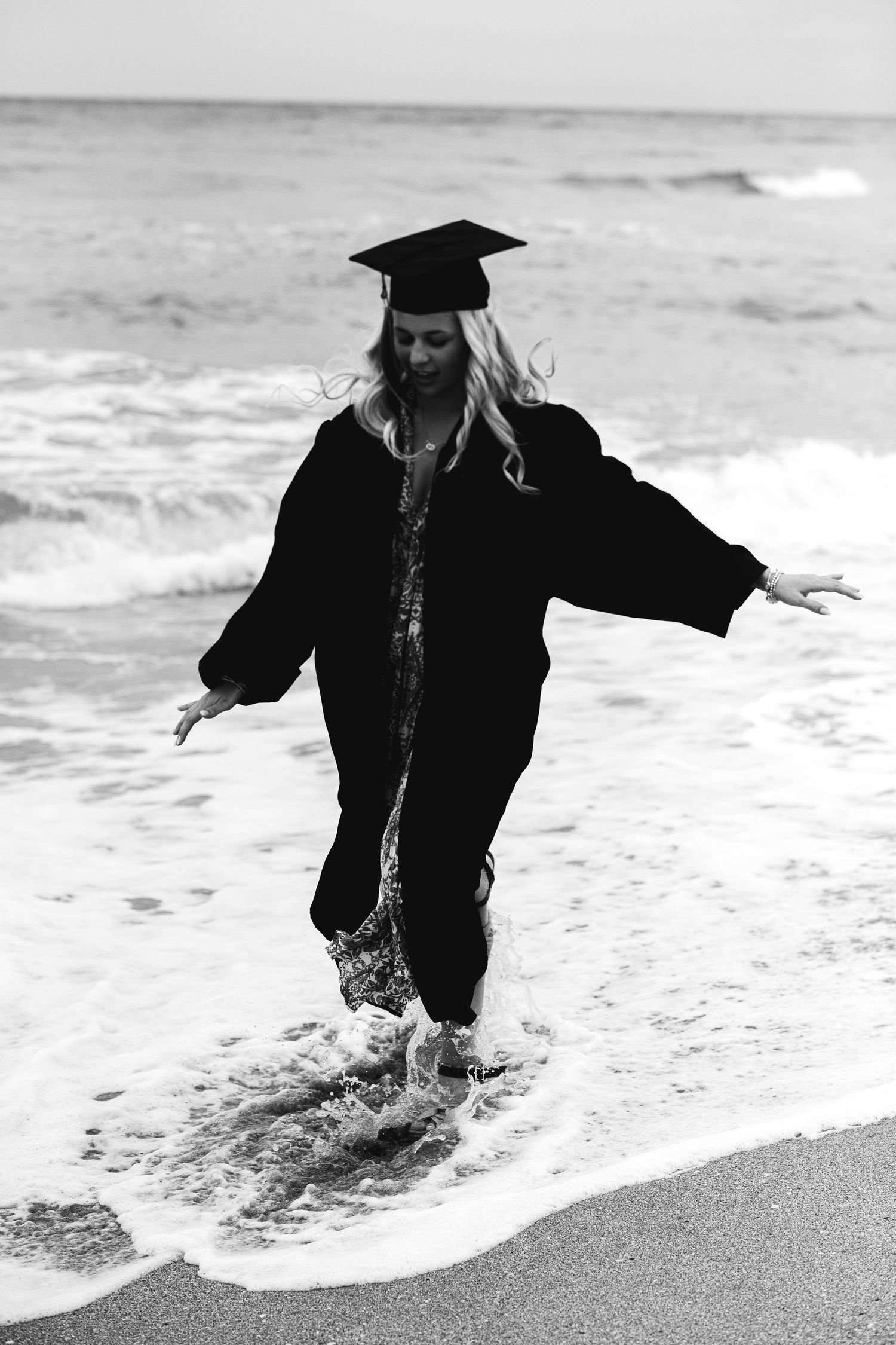 A sequence of black and white photos showing a person in graduation attire splashing in ocean waves.