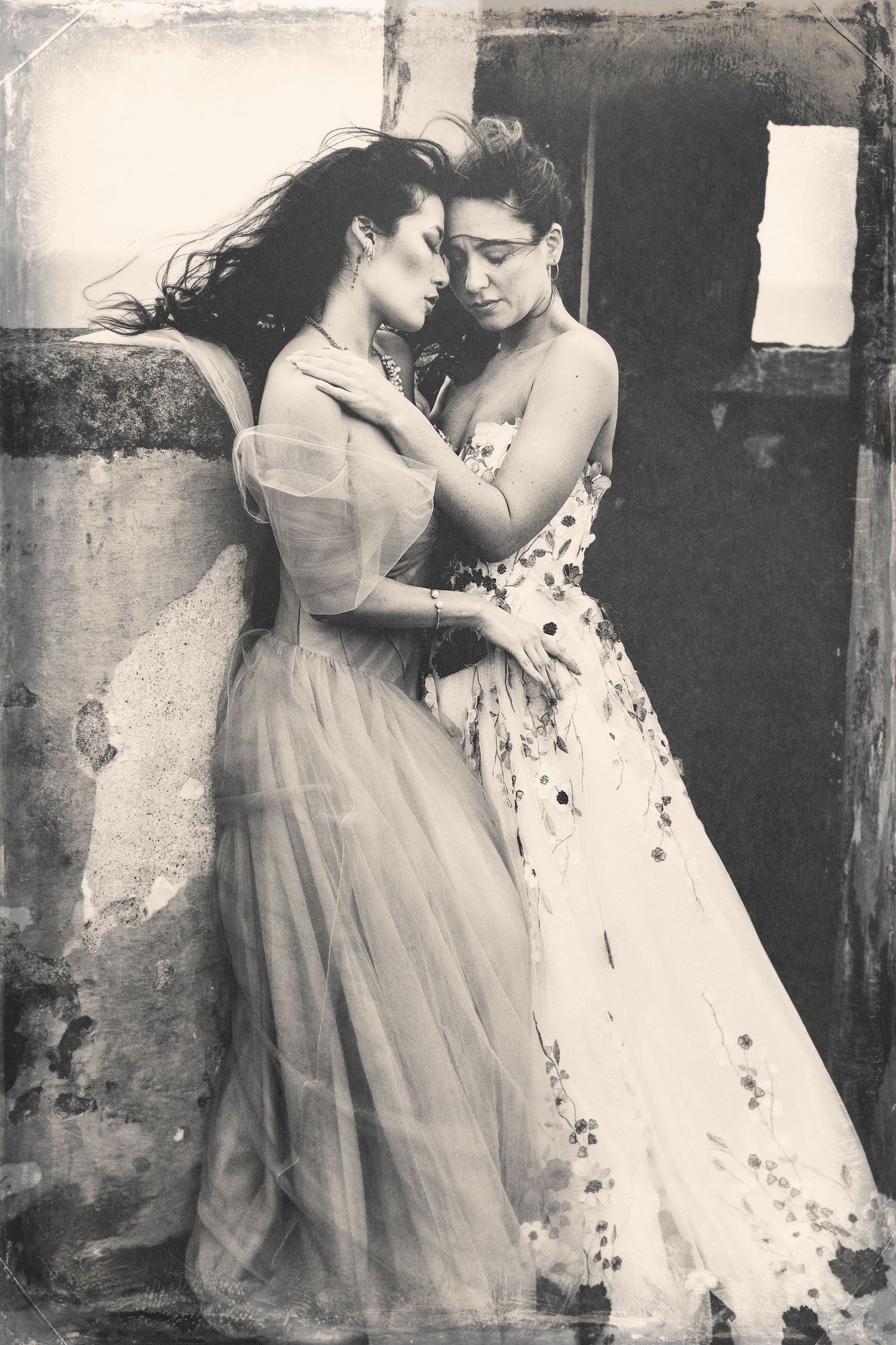 Two figures in elegant dresses share an intimate moment in a vintage-style black and white portrait.