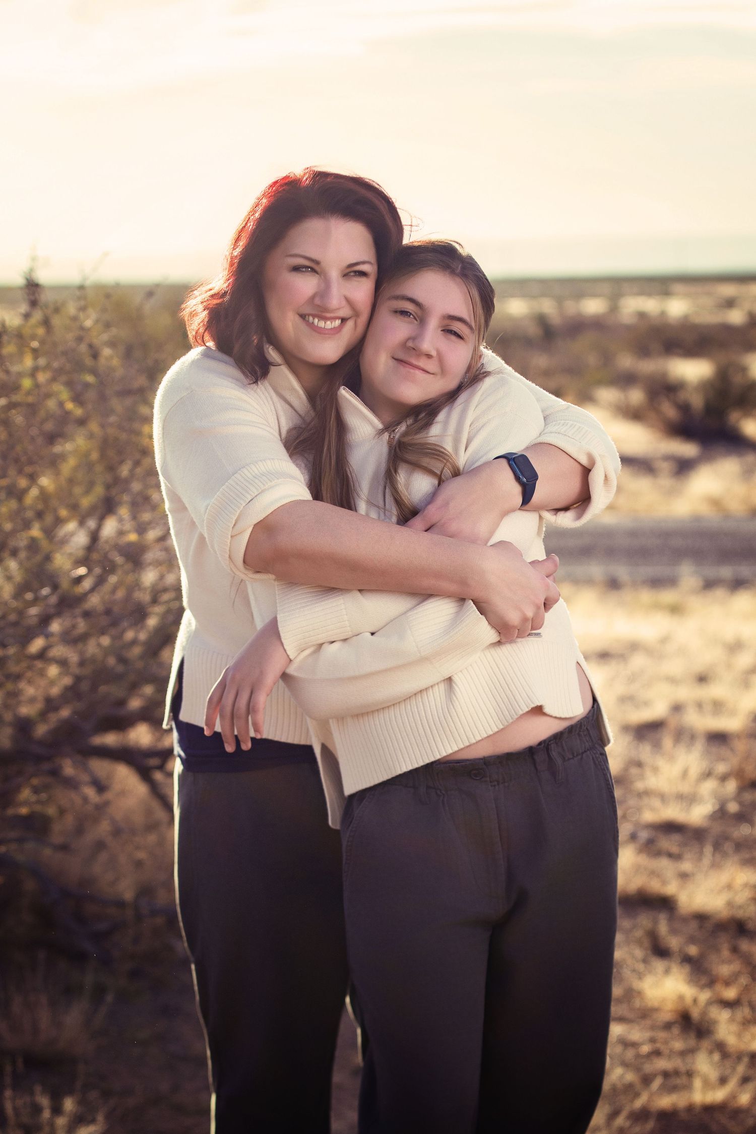 Candid outdoor portrait of two people hugging and smiling in cream colored sweaters at sunset.