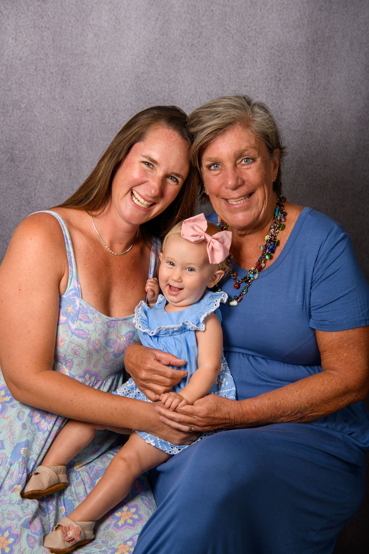 A heartwarming family portrait showing three generations sharing loving embraces against a grey backdrop.