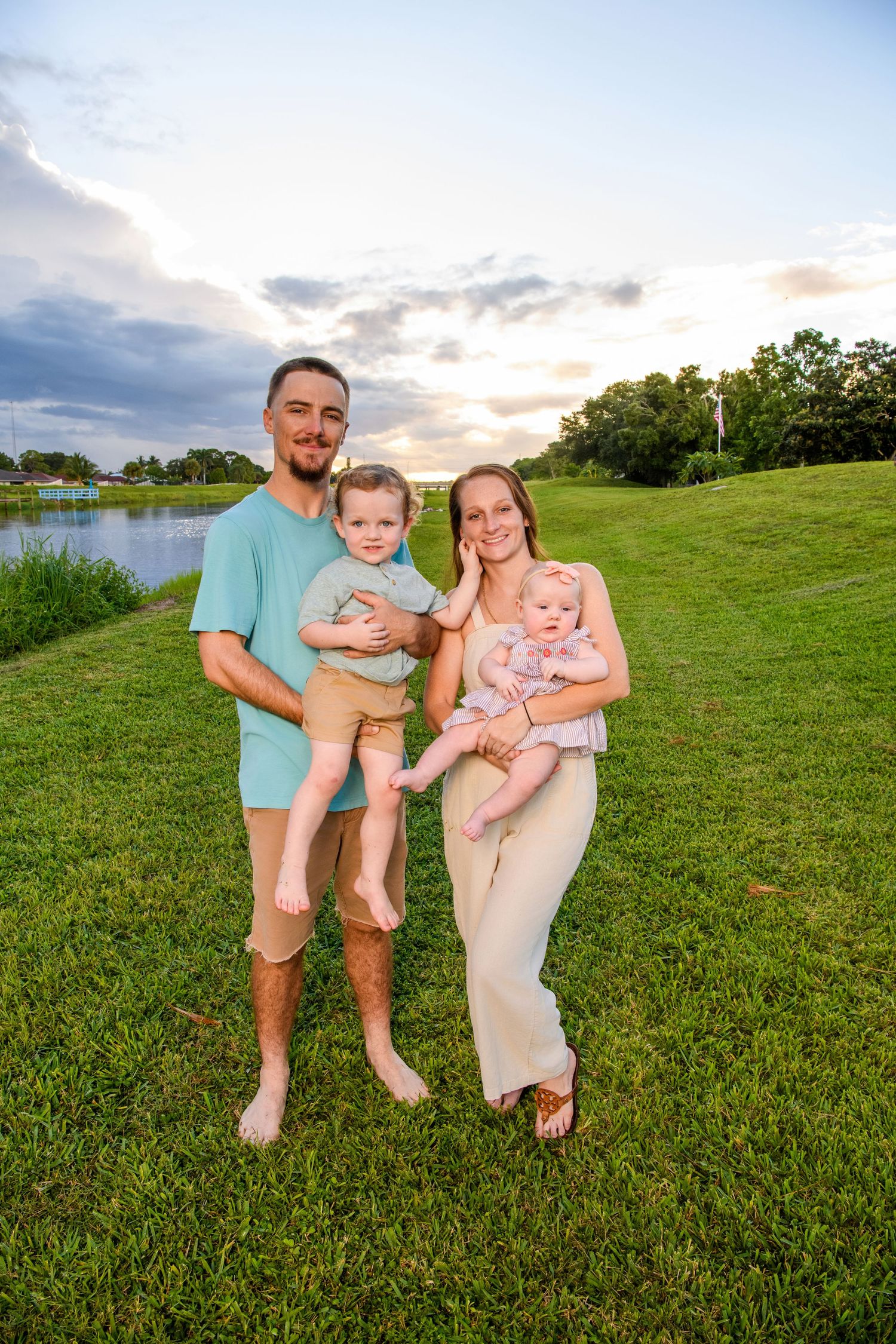 Young family poses together on grassy hillside during golden hour.