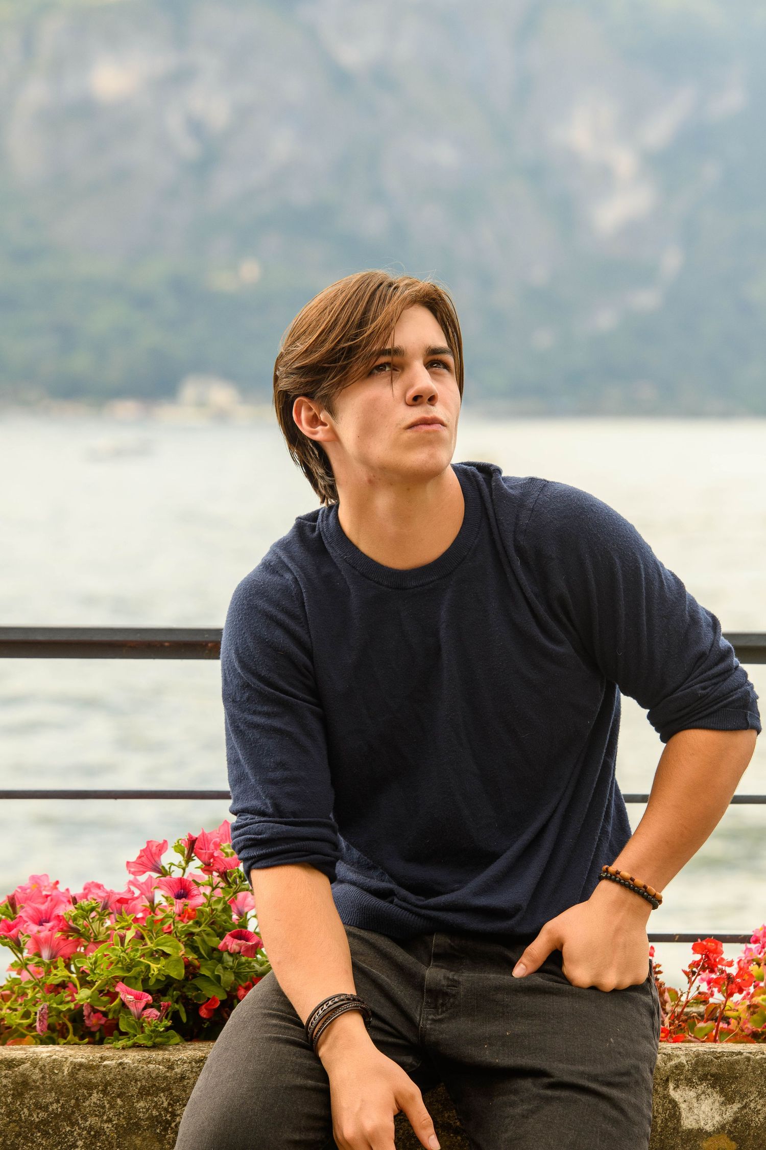 Person in dark shirt looking out over scenic mountain lake with flowers in foreground.
