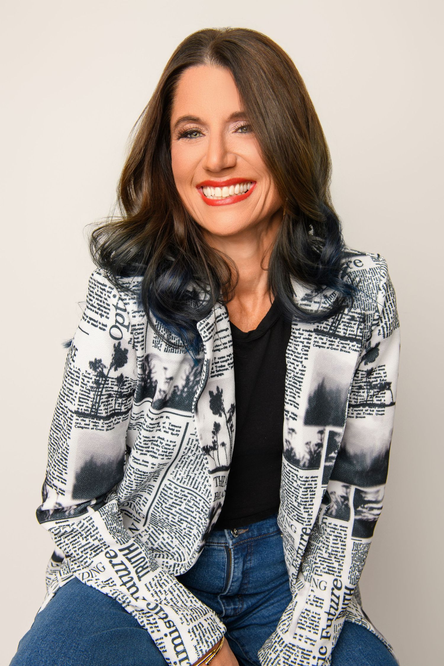 Casual studio photo featuring a newspaper print jacket paired with jeans and black top.