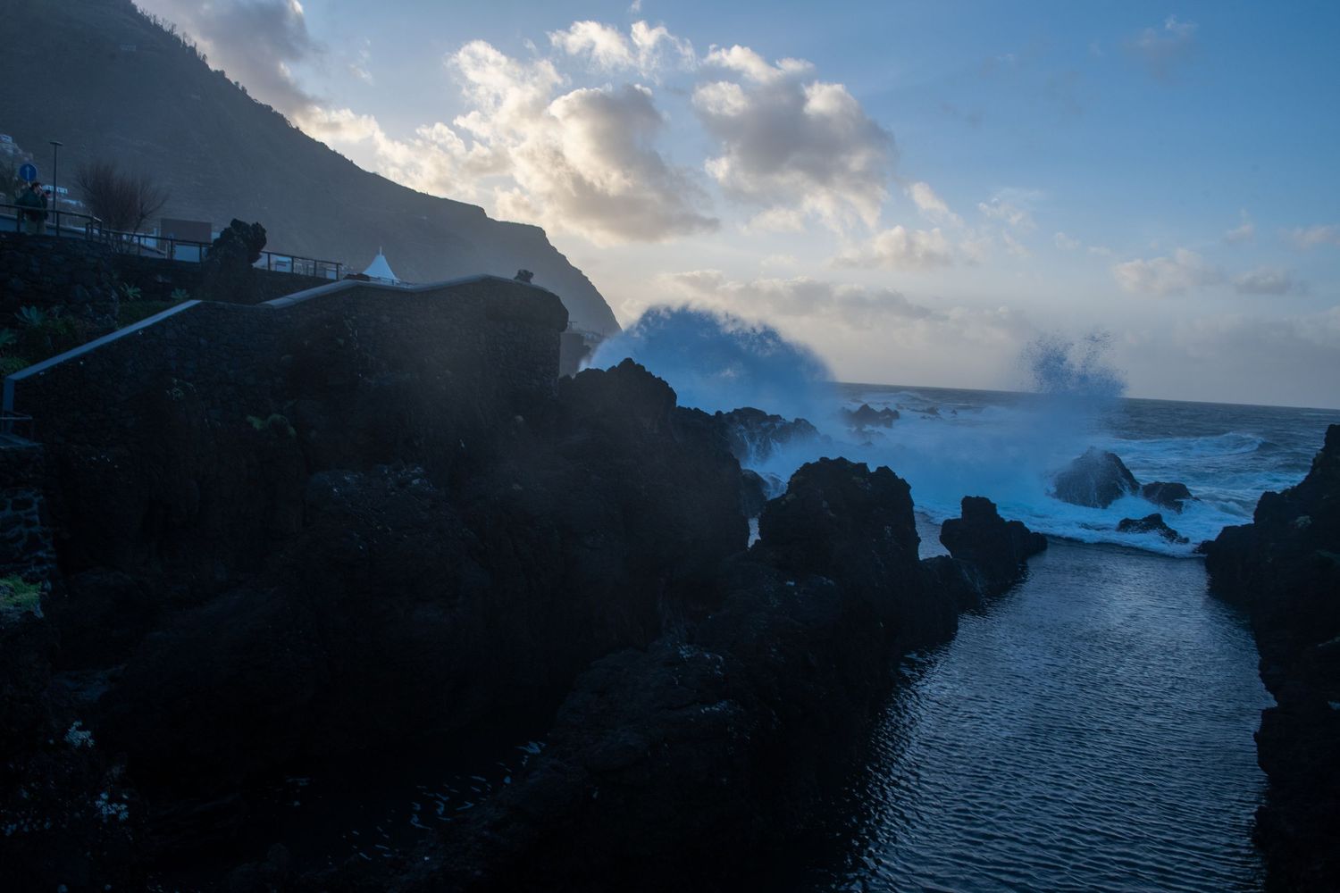 Moody coastal scene at dusk with dark rocky formations and misty ocean waves.