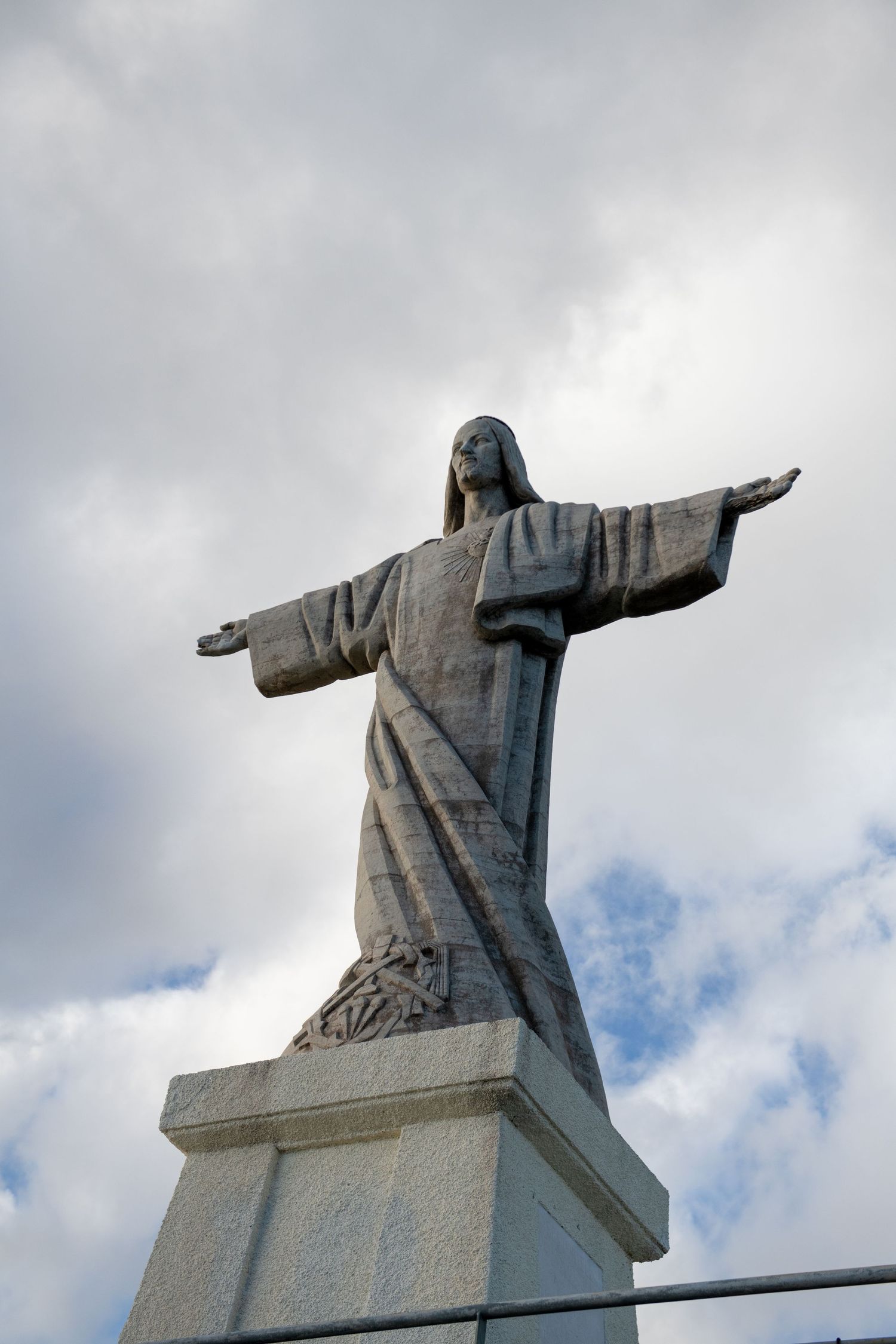 Christ the Redeemer statue stands against cloudy sky with outstretched arms in dramatic pose.