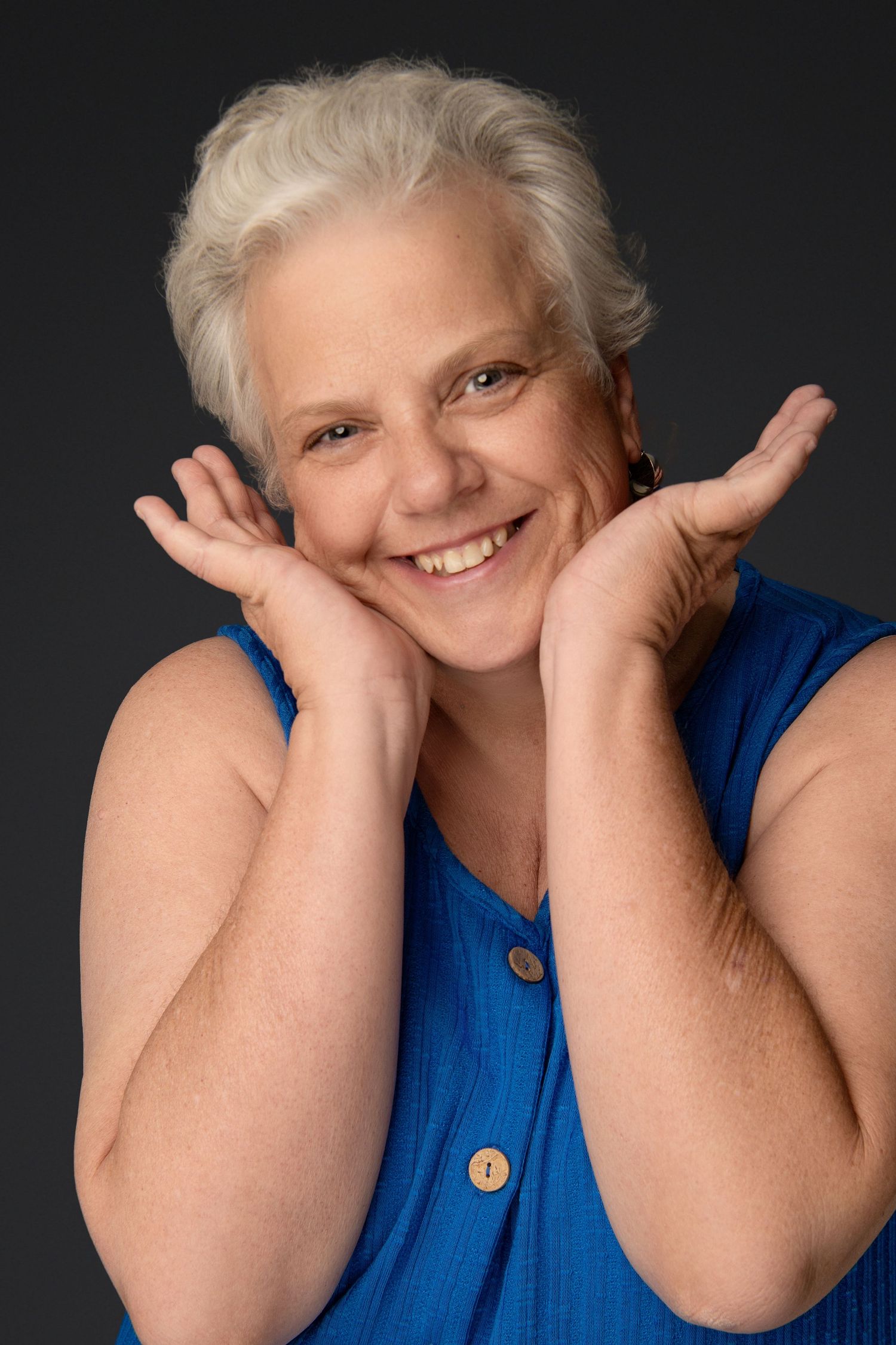 Fun Close-up portrait of woman in her 50's in blue tank top with hands framing face.