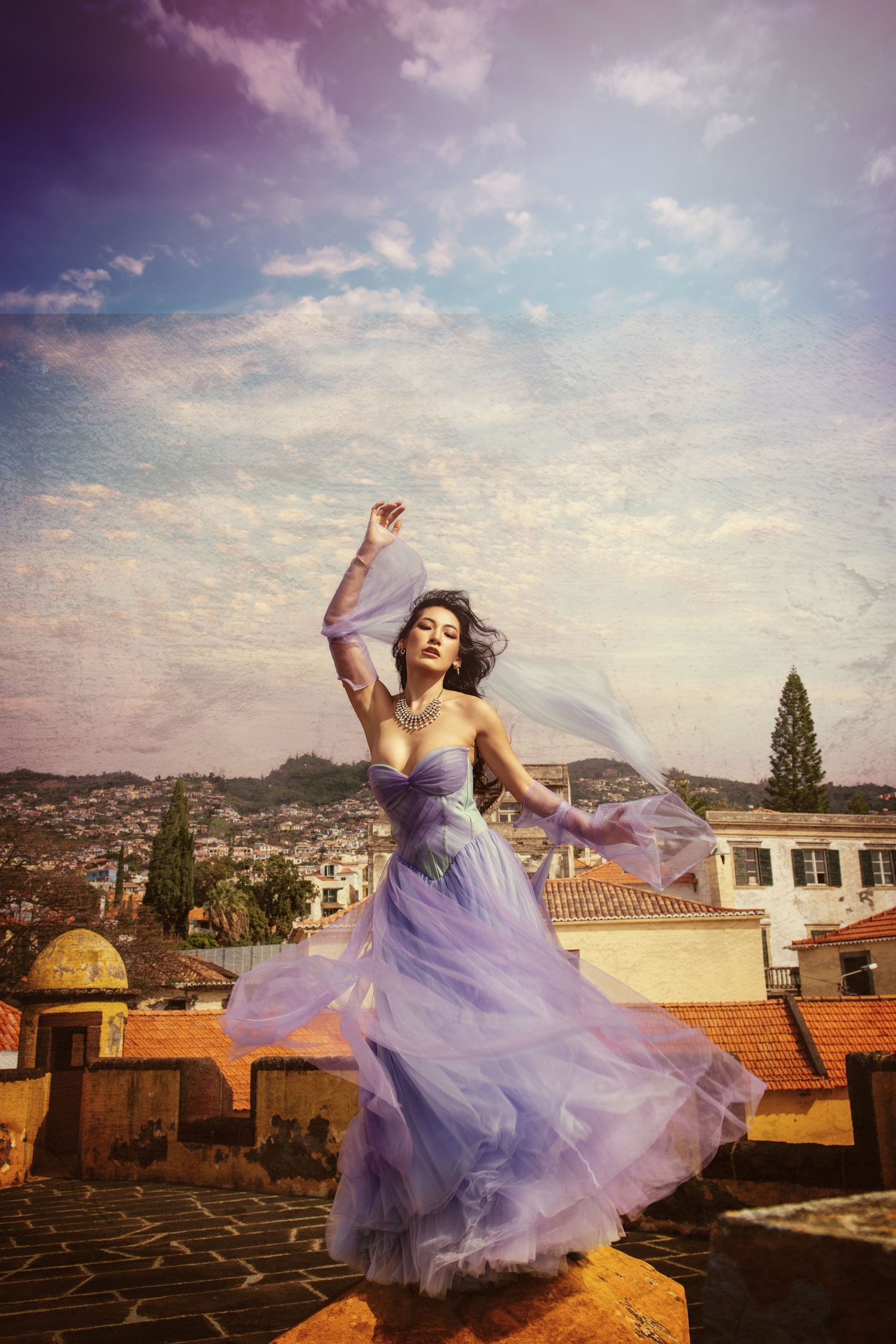 Whimsical portrait in purple dress dancing on rooftop against sunset sky.