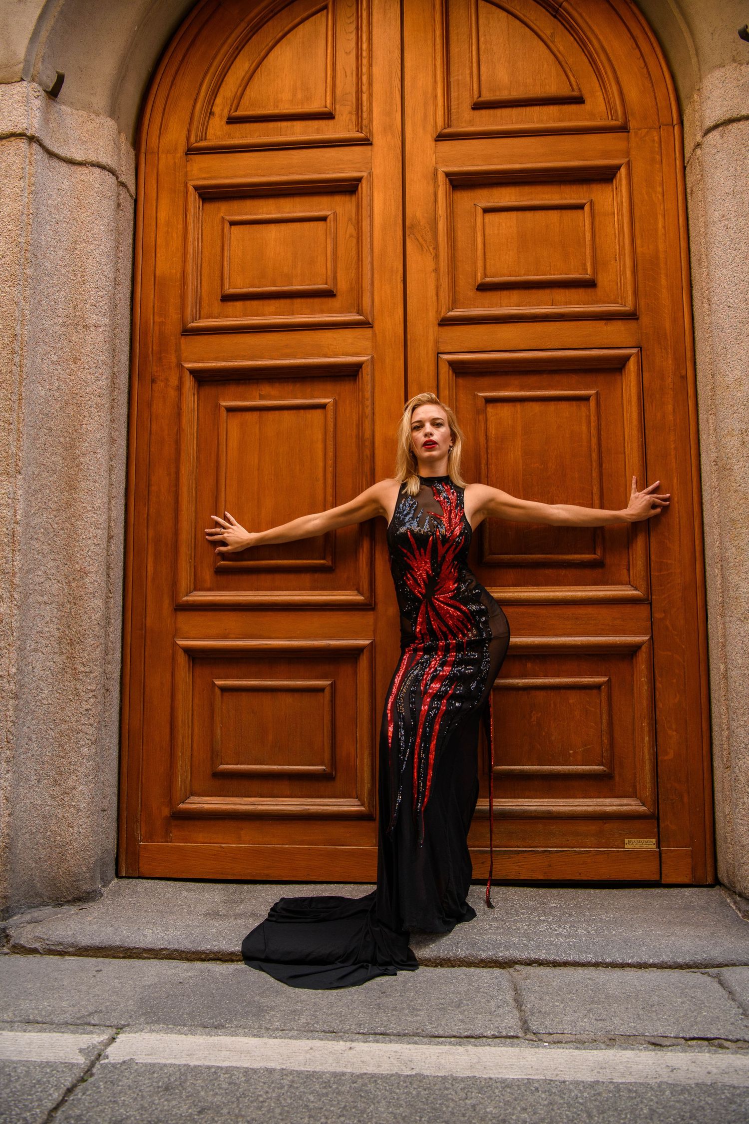 Dramatic black and red gown posed against large wooden door in classic architecture.
