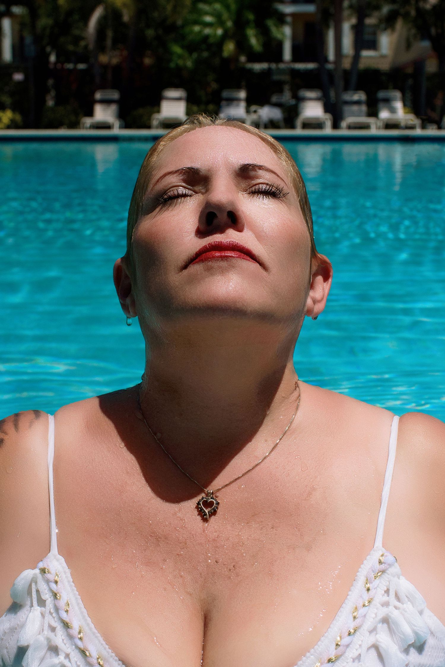 Woman in white swimwear relaxing by a bright blue swimming pool on a sunny day.