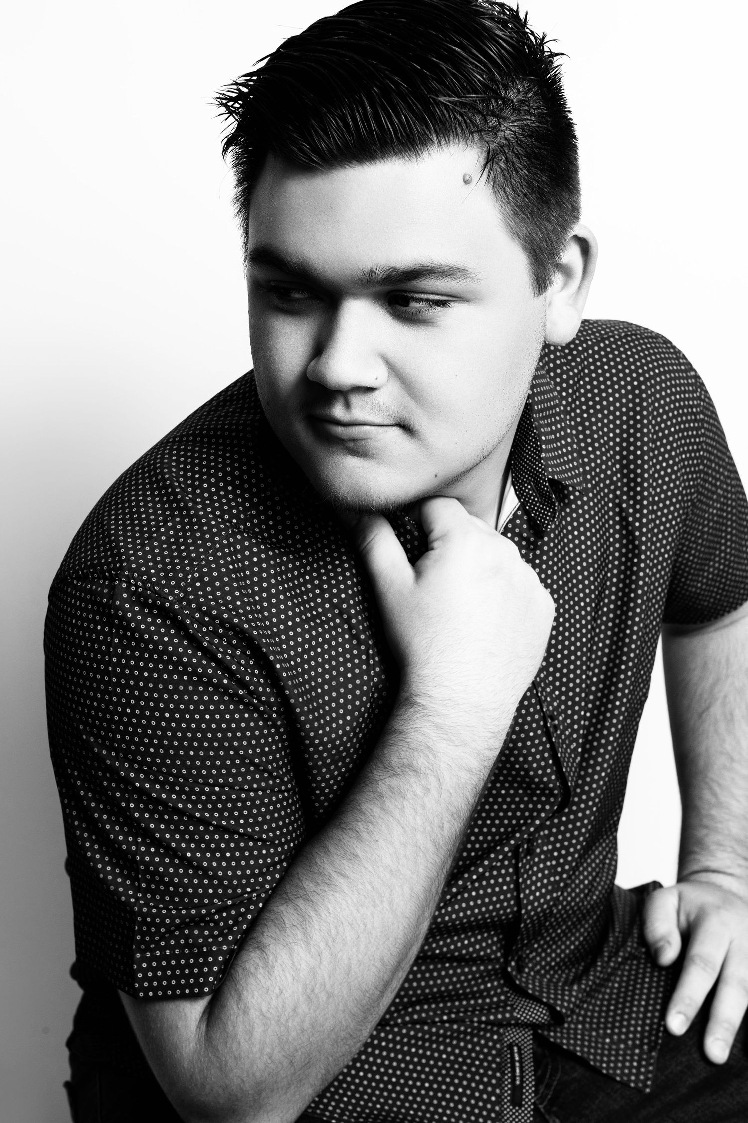 Professional portrait of a young man in a polka dot shirt against a white background.