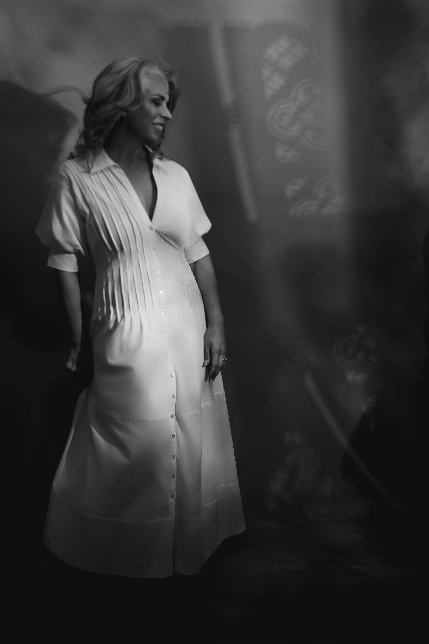 Artistic black and white portrait of person in white clothing with dramatic shadows.